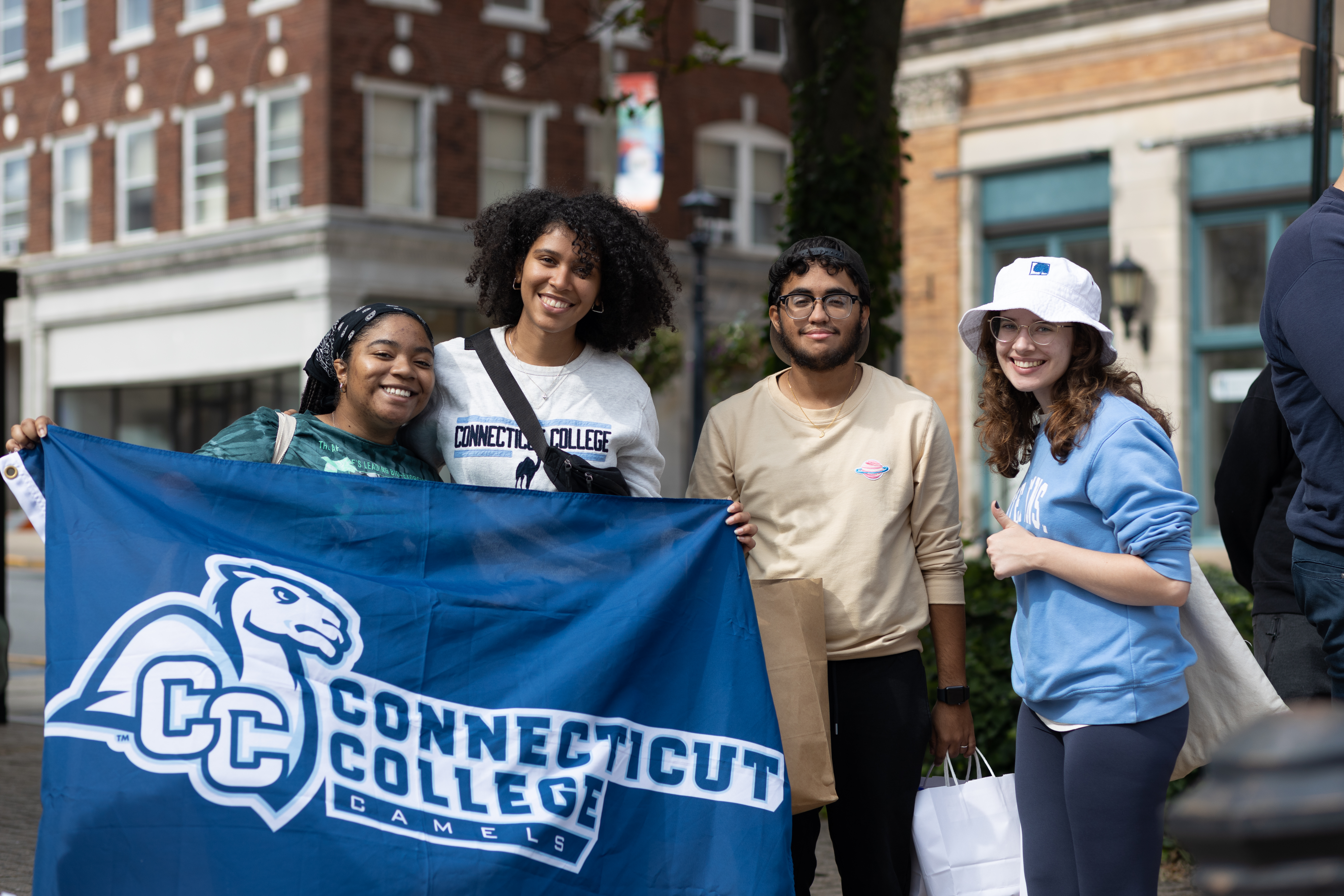 Students posing with a Connecticut College flag at the New London We Are/Nos Somos parade