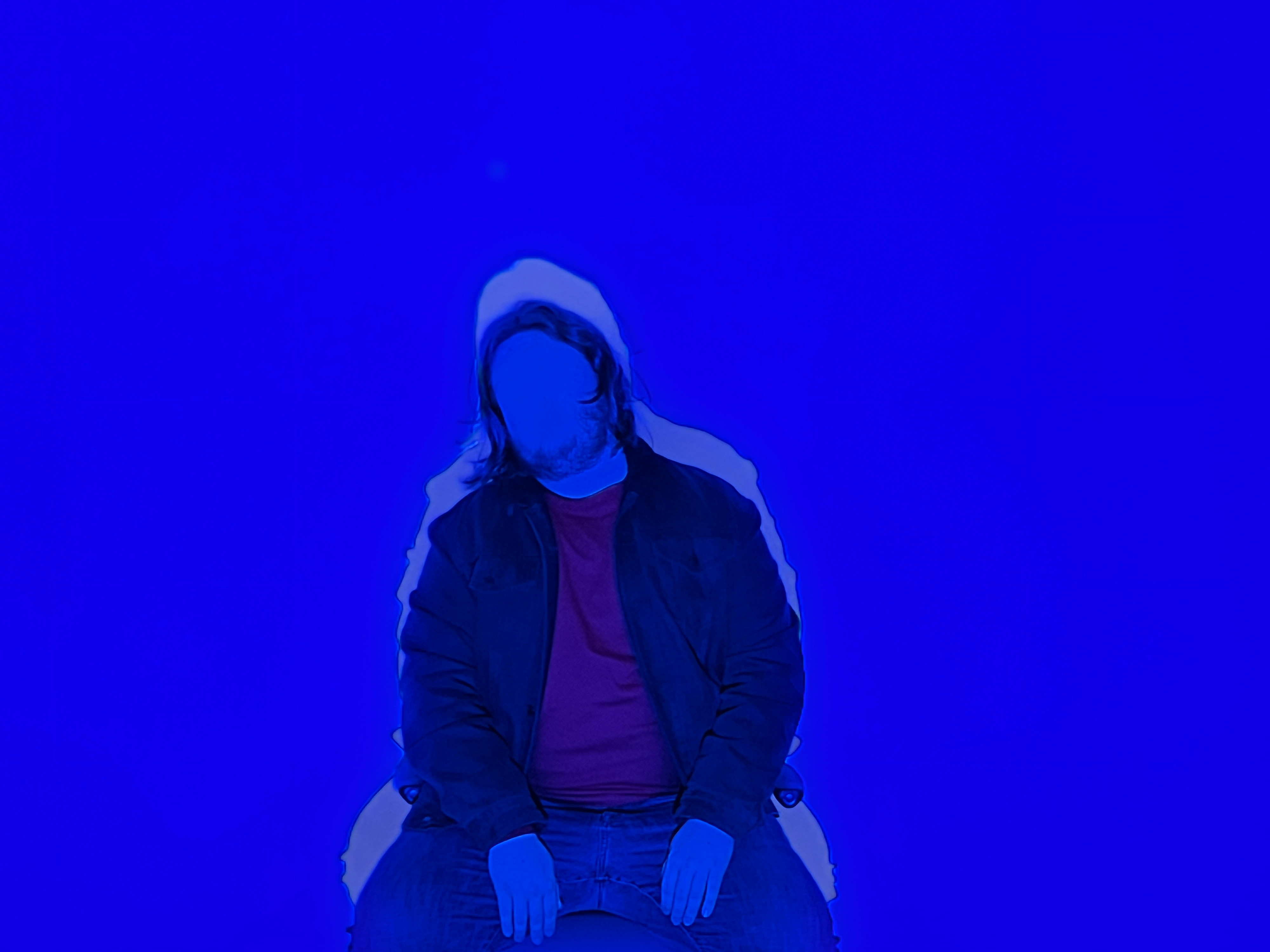 A figure sitting with a blue background and no face.