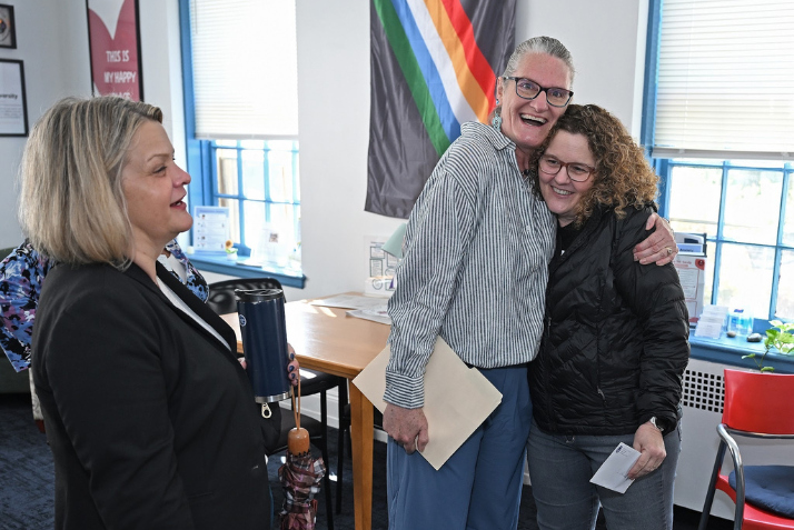 President Andrea Chapdelaine looks on as Merrill Collins hugs Jillian Heilman.
