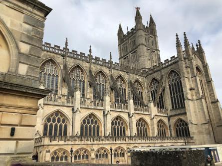A photo of Bath Cathedral, build of smooth stone and arched windows with a tower in the background