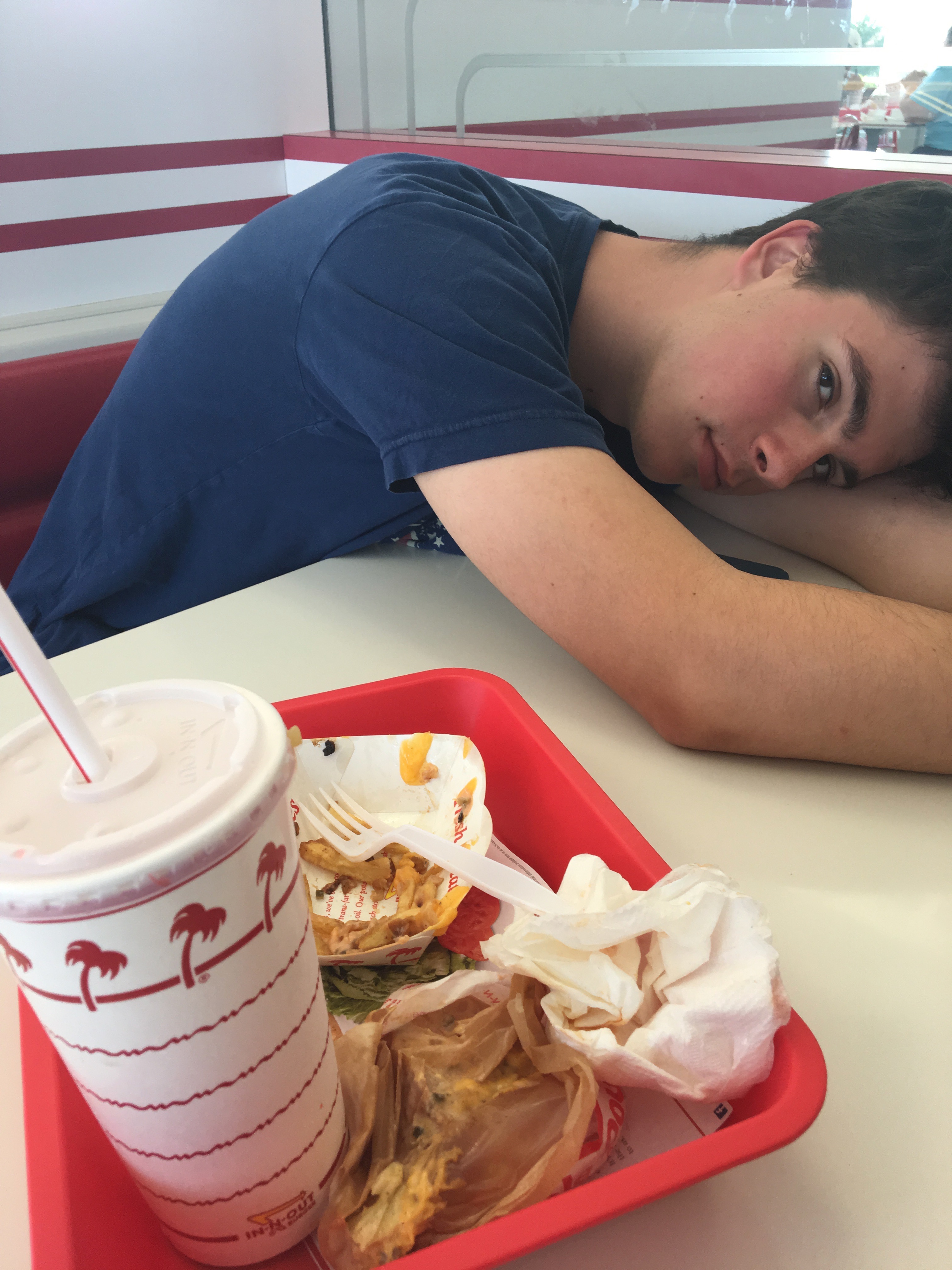 Samuel rests his head on the table next to the remains of his lunch from In-N-Out Burger.