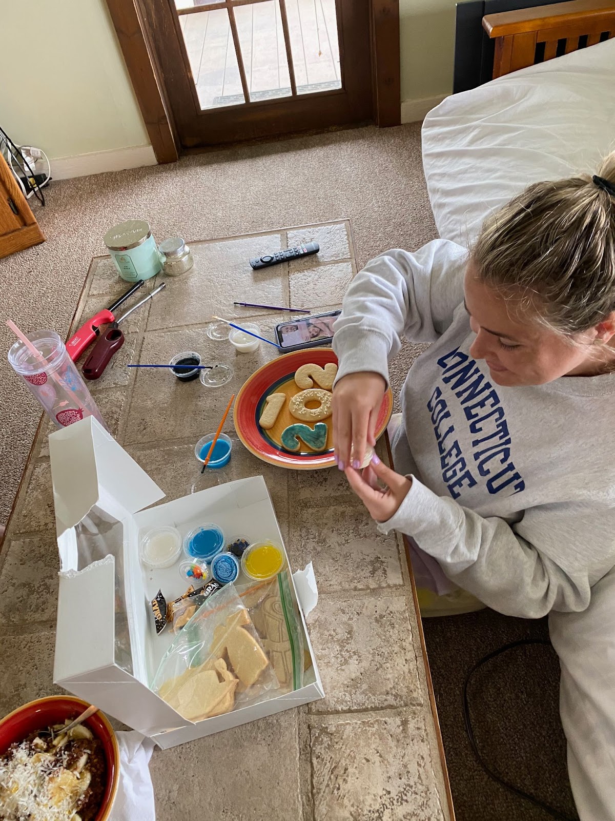Student with a Connecticut College shirt on decorates cookies with colored frosting.