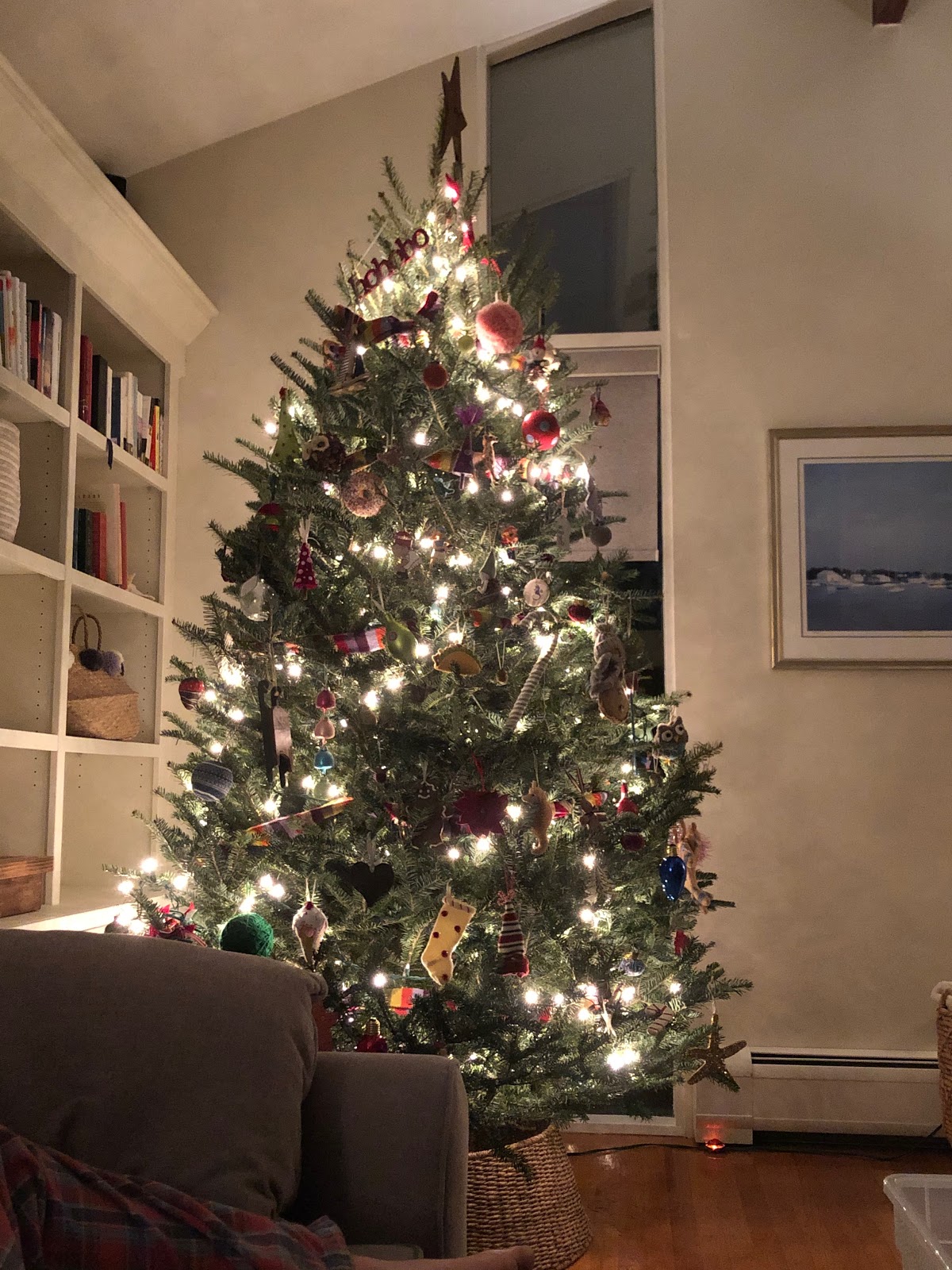 A Christmas tree stands alight in the corner of a living room in front of a comfy armchair