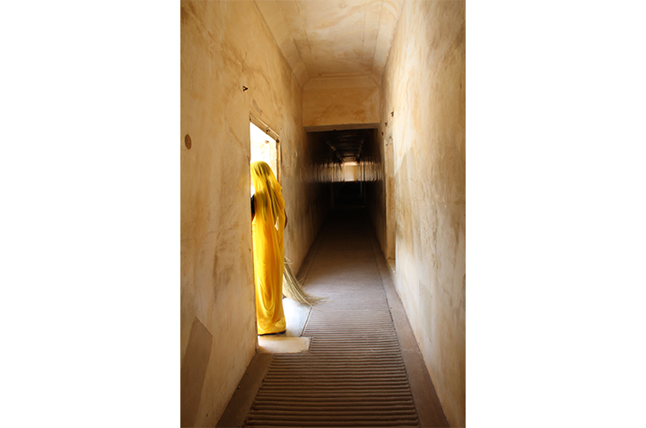 Woman in yellow gazing out a doorway in a dark hall