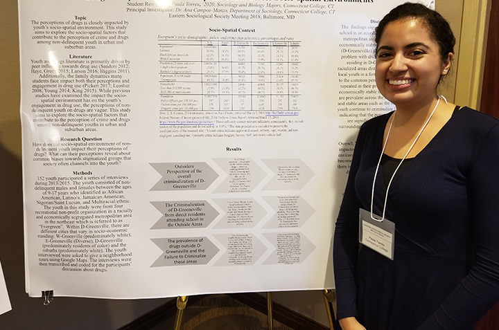 A sociology student stands with her presentation at a conference. 