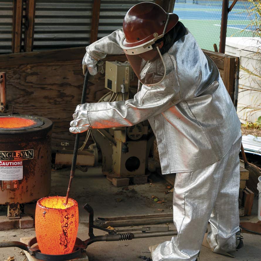 image of student in heat suit stirring an aluminum mold to create a sculpture