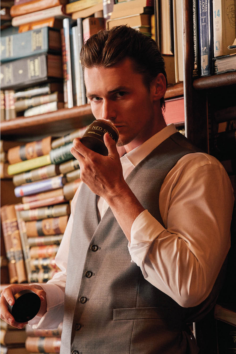 Image of model smelling jar of Crowned Skin product in front of bookcase