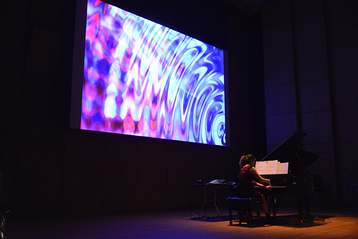 A woman plays piano as art is projected behind her