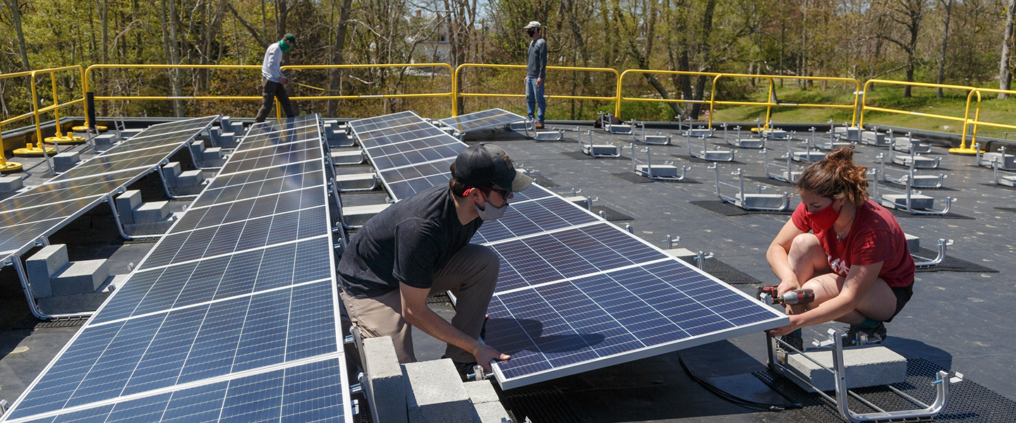Students help install solar panels onto a building roof. 