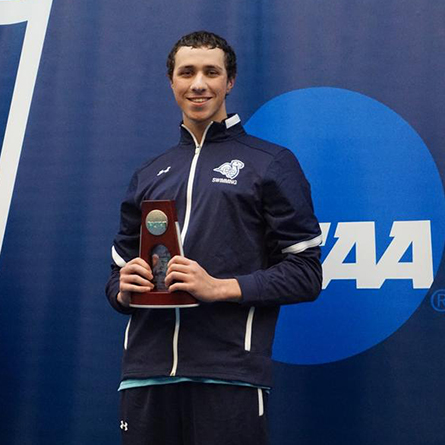Justin Finkel ’25 holds an NCAA trophy at the men's swimming national championship meet.