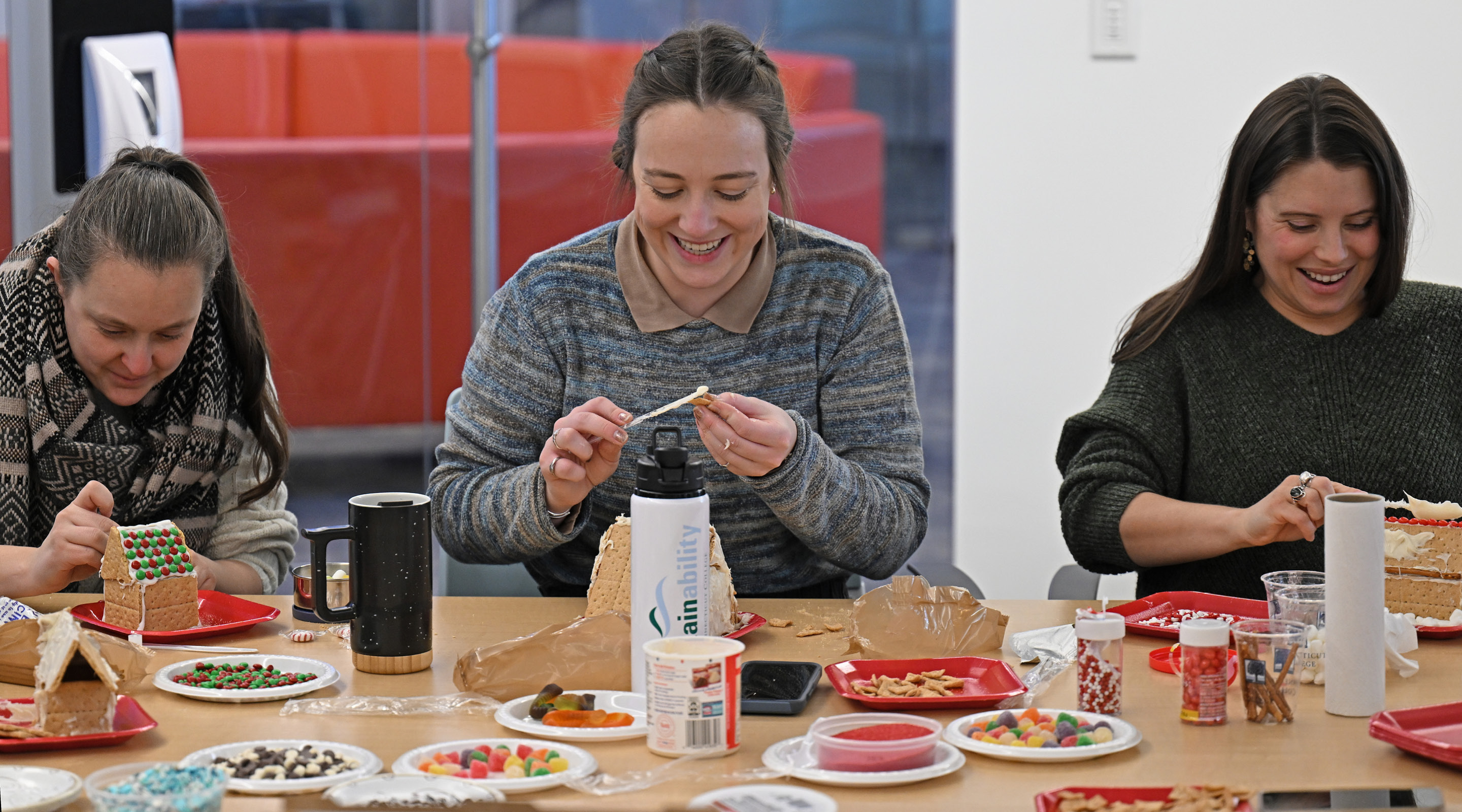 Margaret Bounds, Director of Sustainability, left, Ashlyn Healey,  Director Summer Programs,  center, and Cara Masullo Ekwuabu, Director CISLA Operations, work on their candy house creations during the Global/Local Engagement Council (GLEC) Holiday party