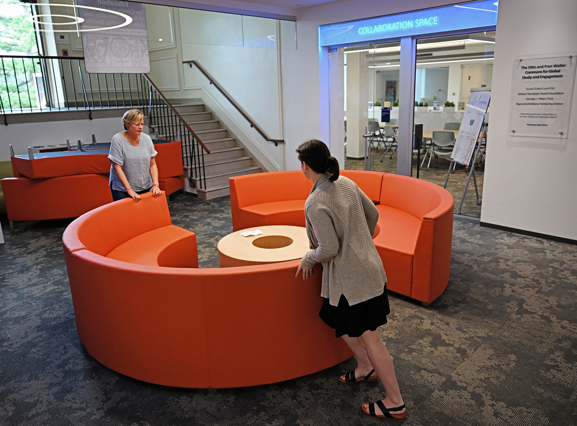 Two college staffers adjust the positioning of a circular couch