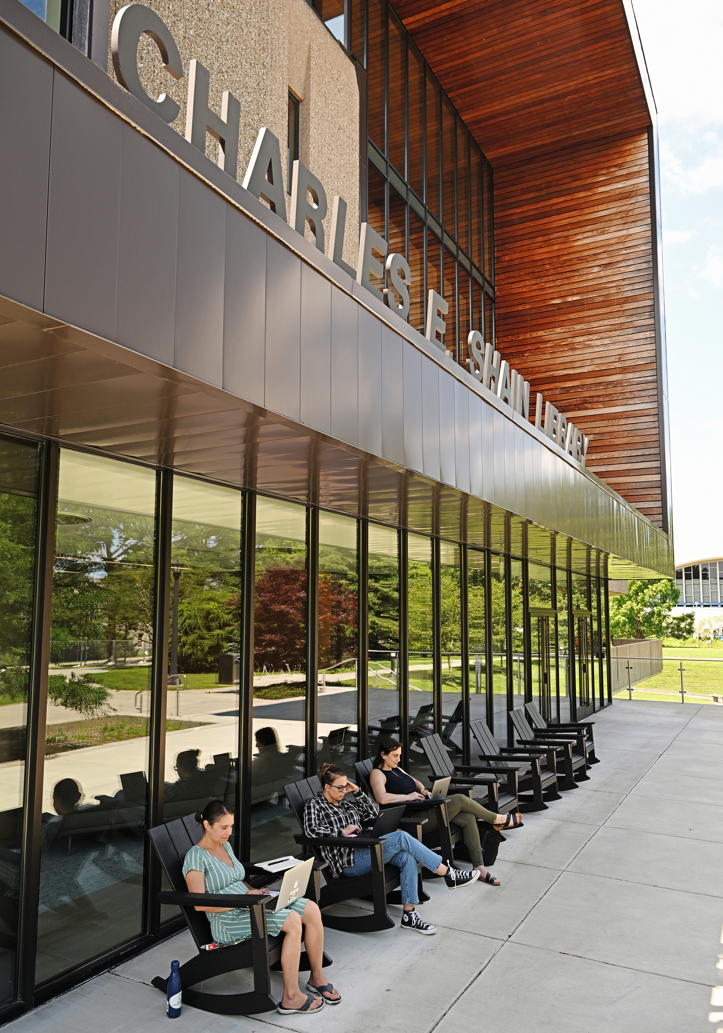 college employees sit in the shade on rocking patio chairs.
