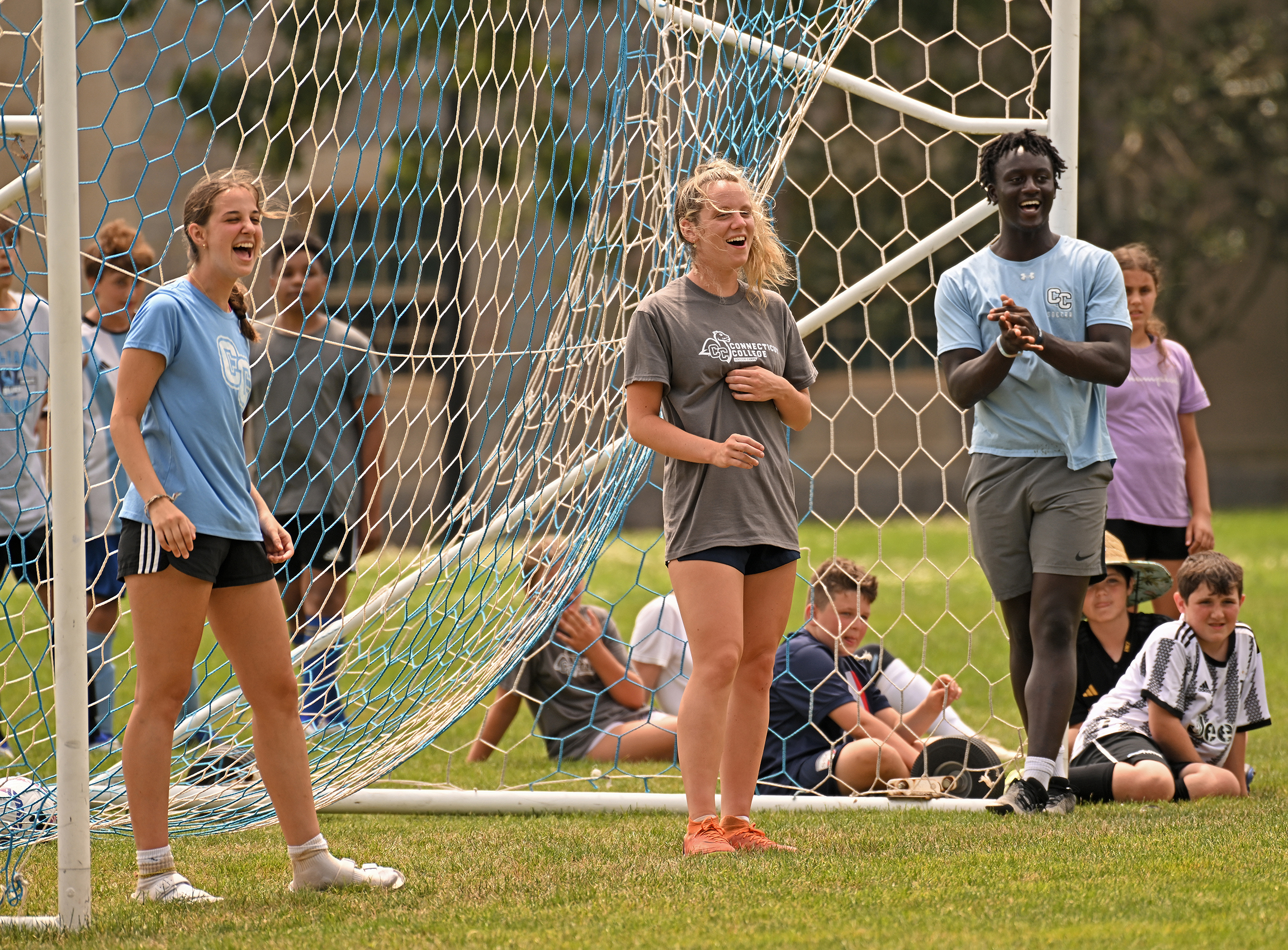 Soccer camp counselors laugh while standing in a goal