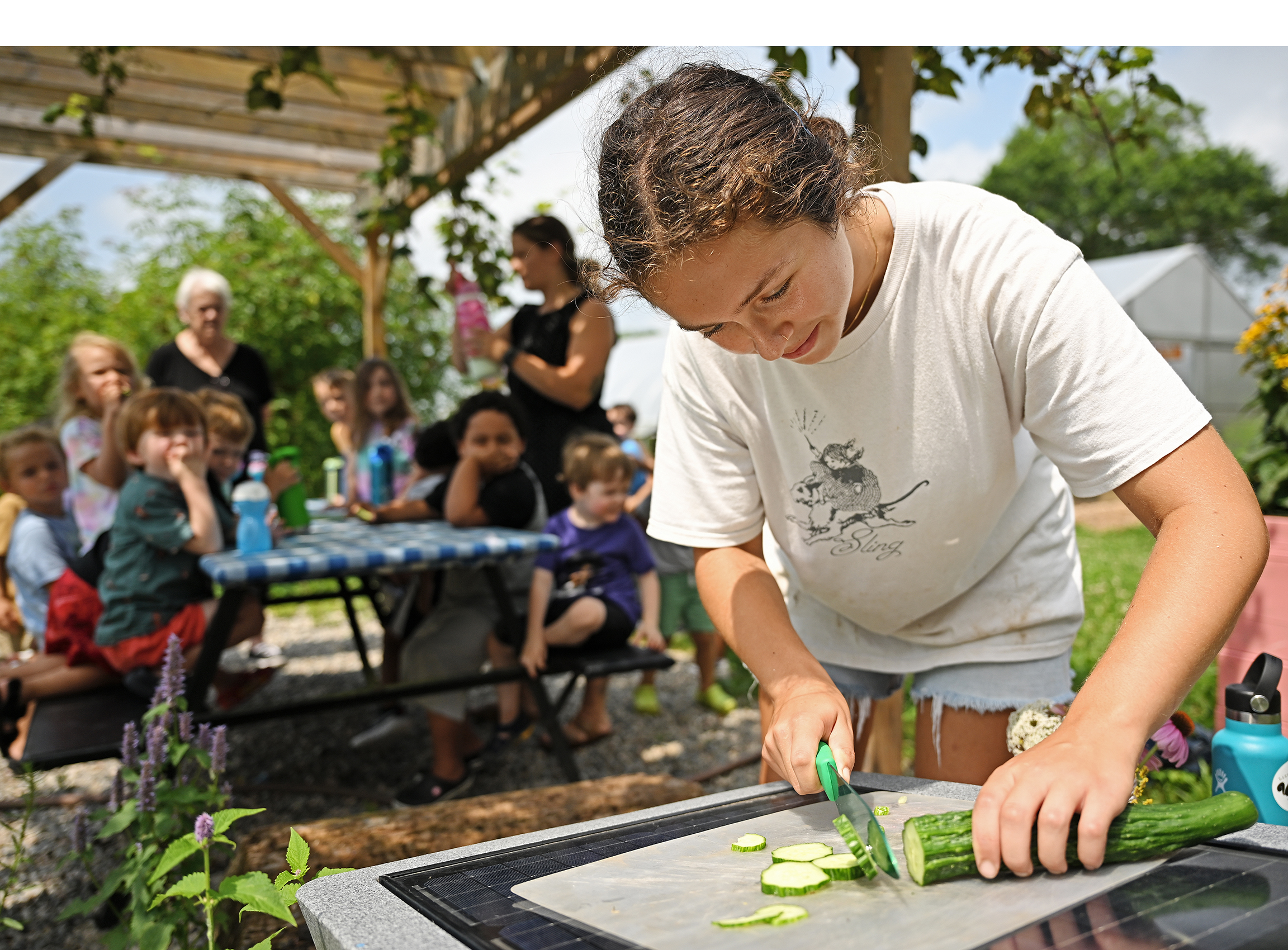 A student gardener slices cucumber while a group of preschoolers watch