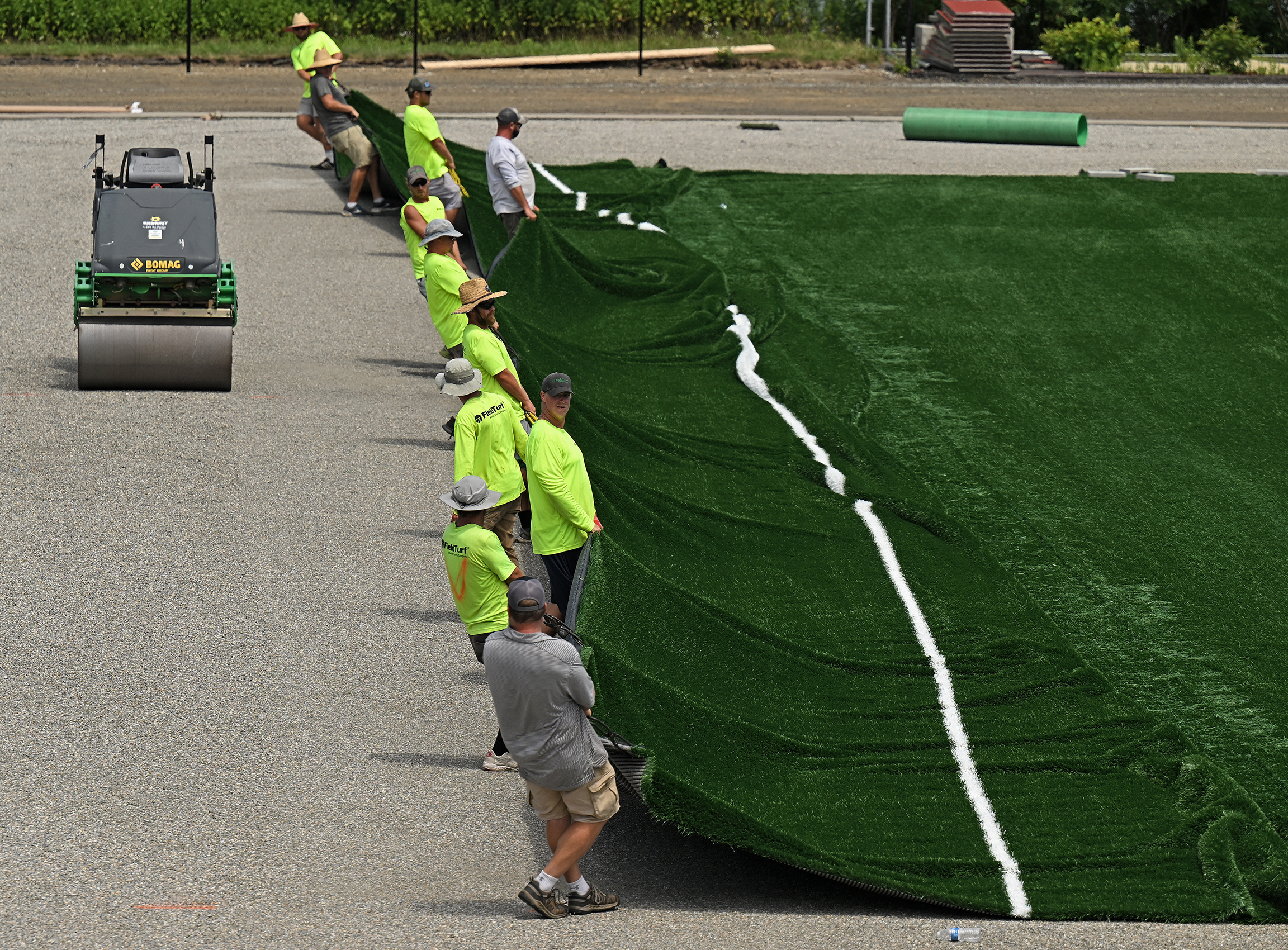 workers drag an artificial turf surface across a field.
