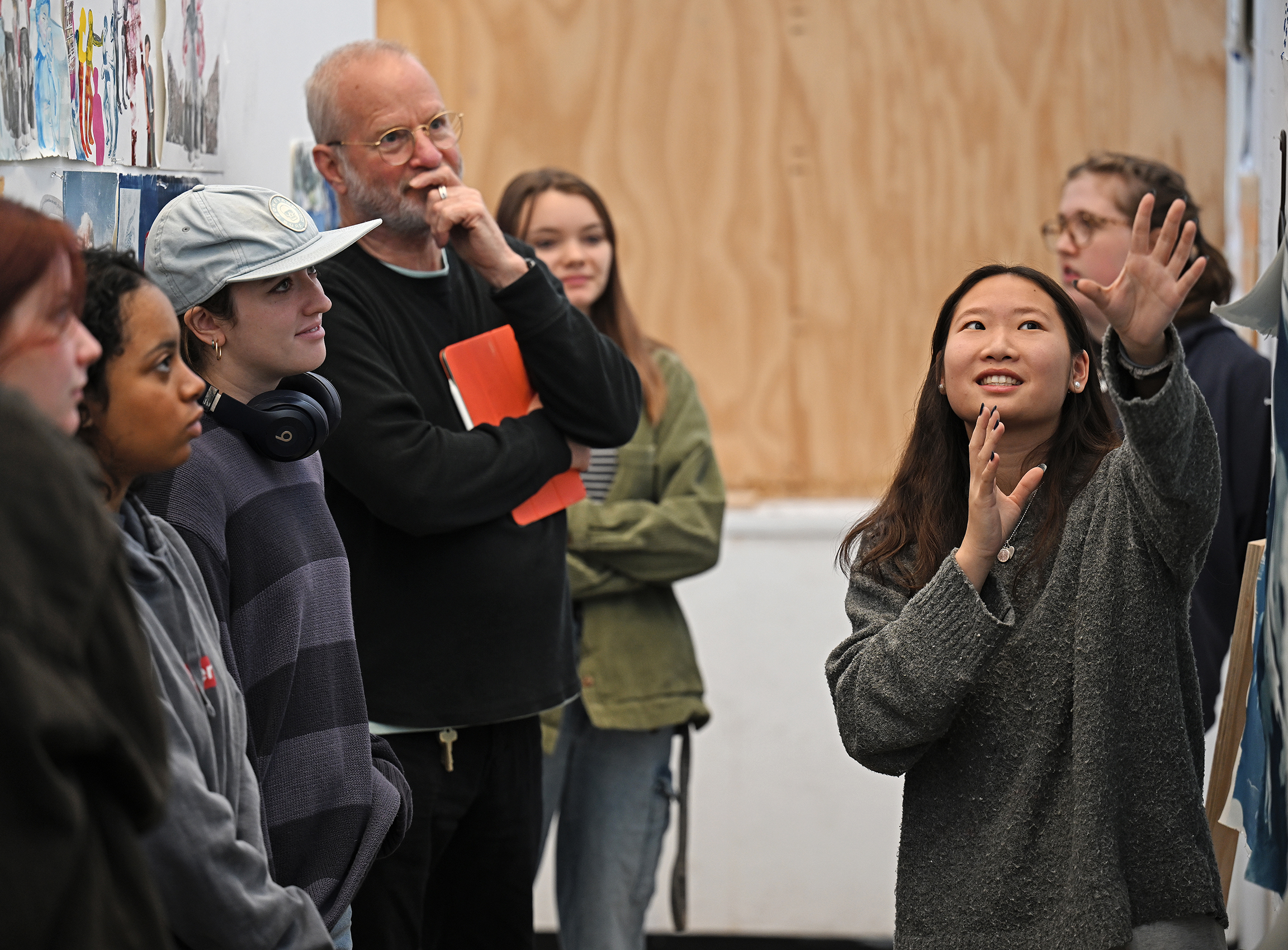 A student gestures to explain their artwork during an art class critique session.