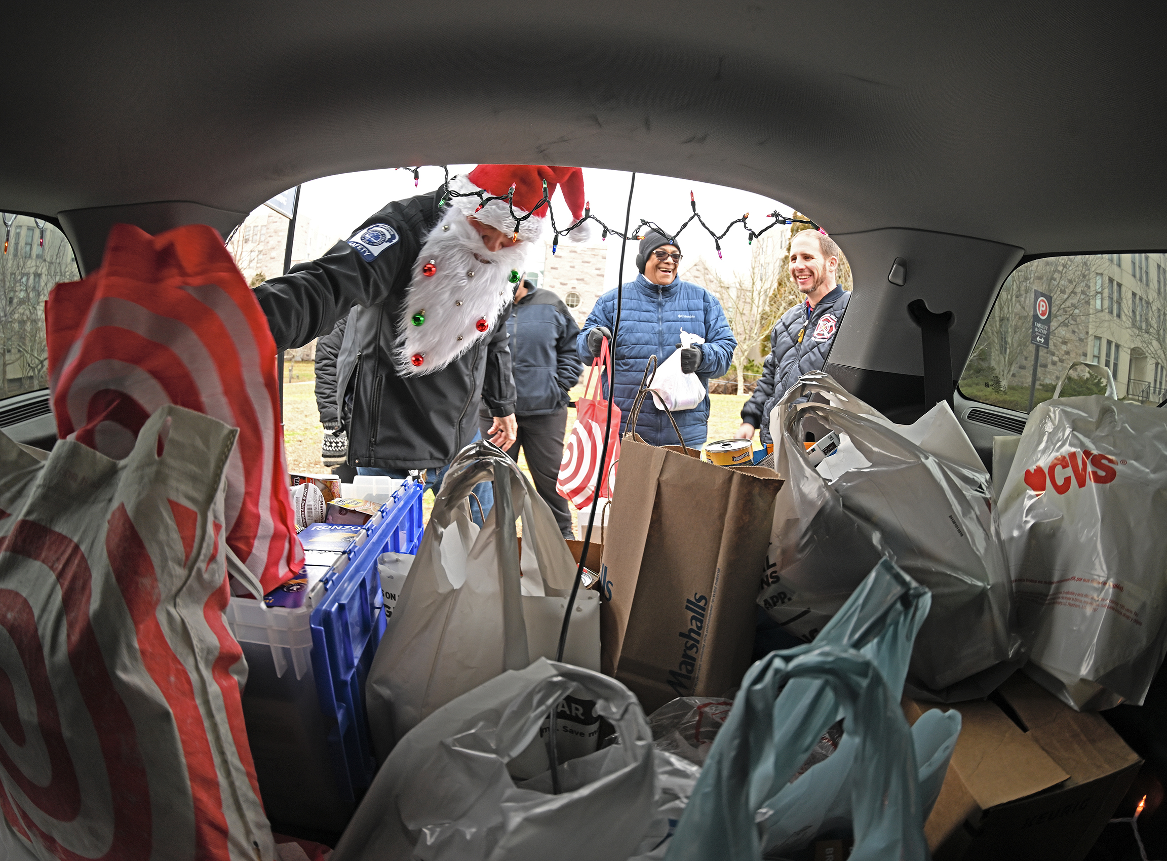 A campus safety officer in santa beard and had adds a bag of donated food to a Stuff-the-Cruiser food drive.