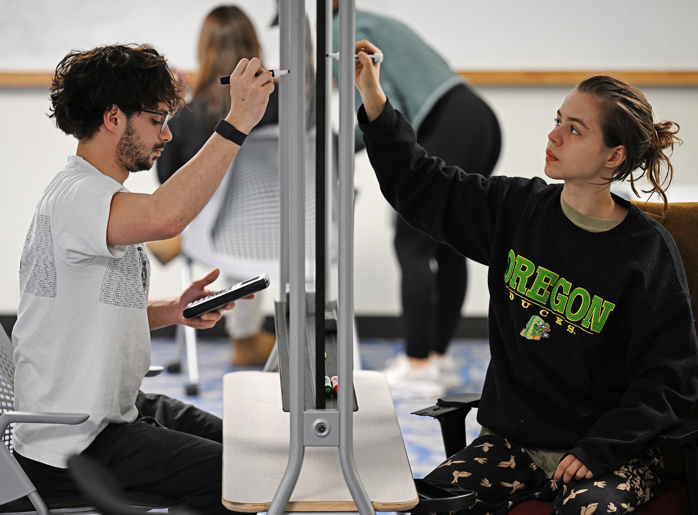 Two students, on either side of a white board, study for finals.