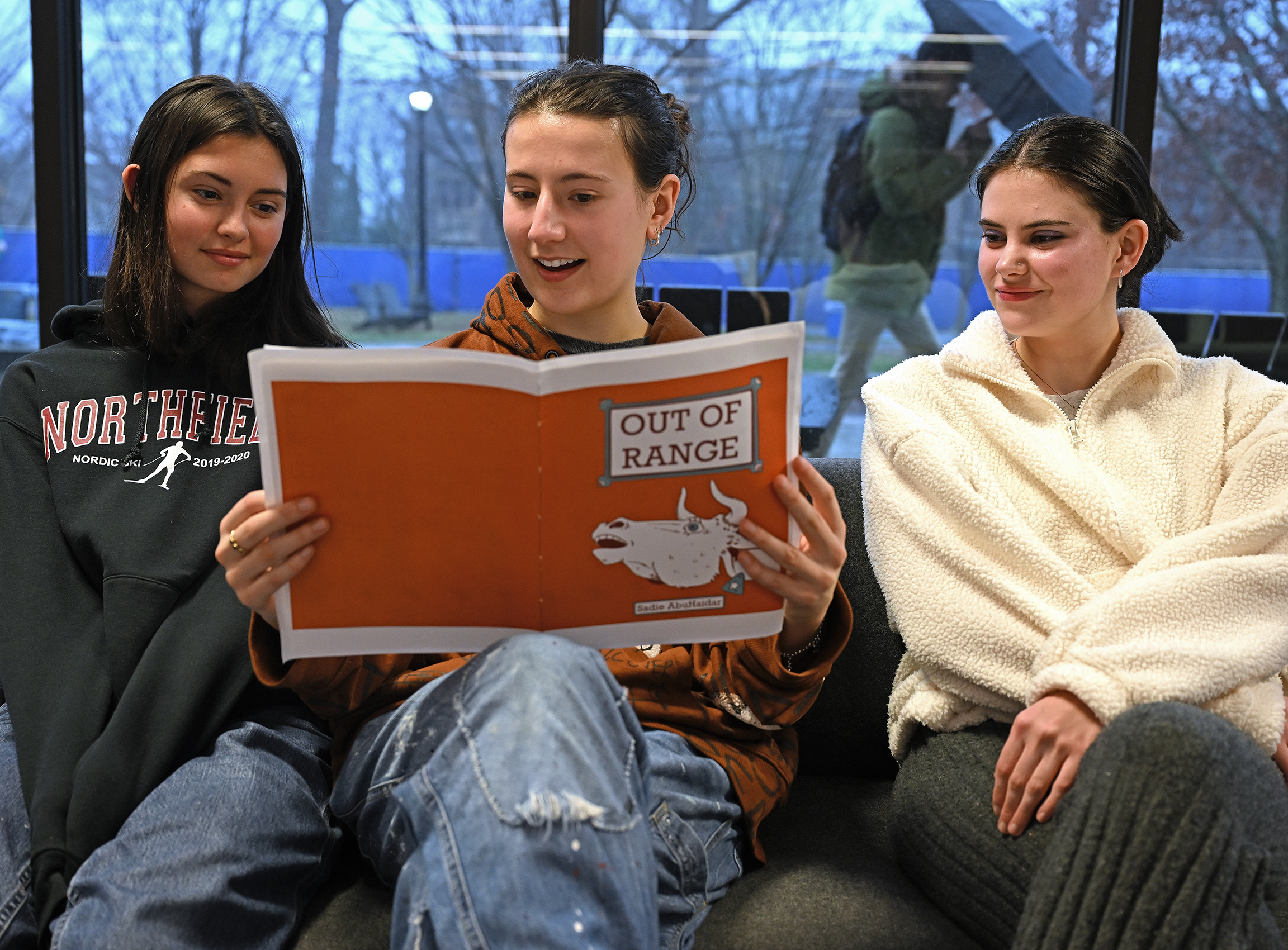 A student sits between two others and reads a comic memoir during an art class critique.