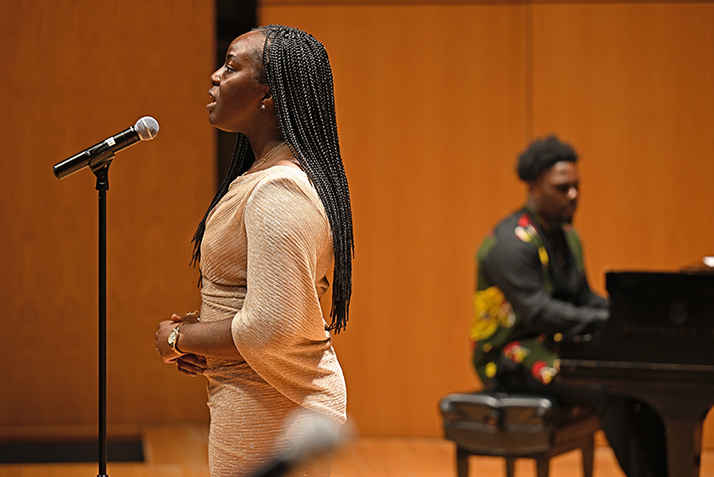 female student sings at microphone with pianist accompanying in the background