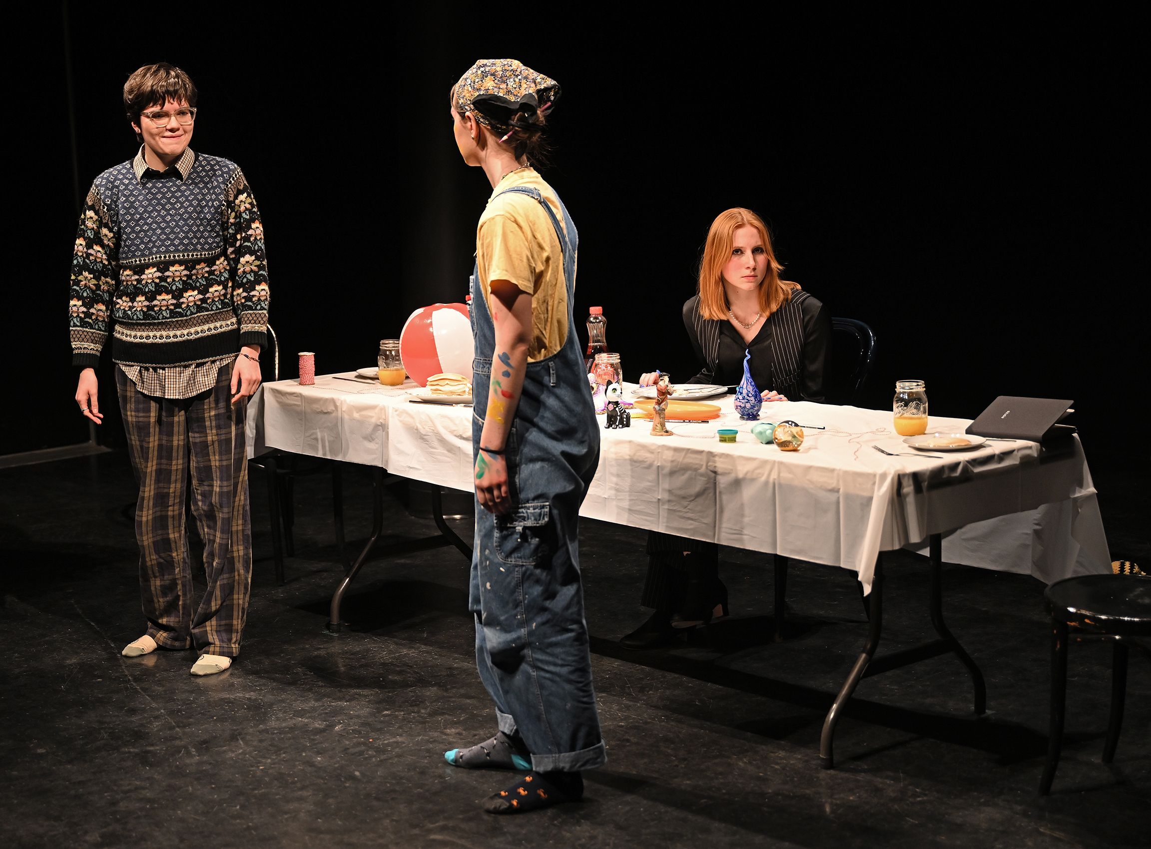 two standing actors speak as another listens while seated at a table