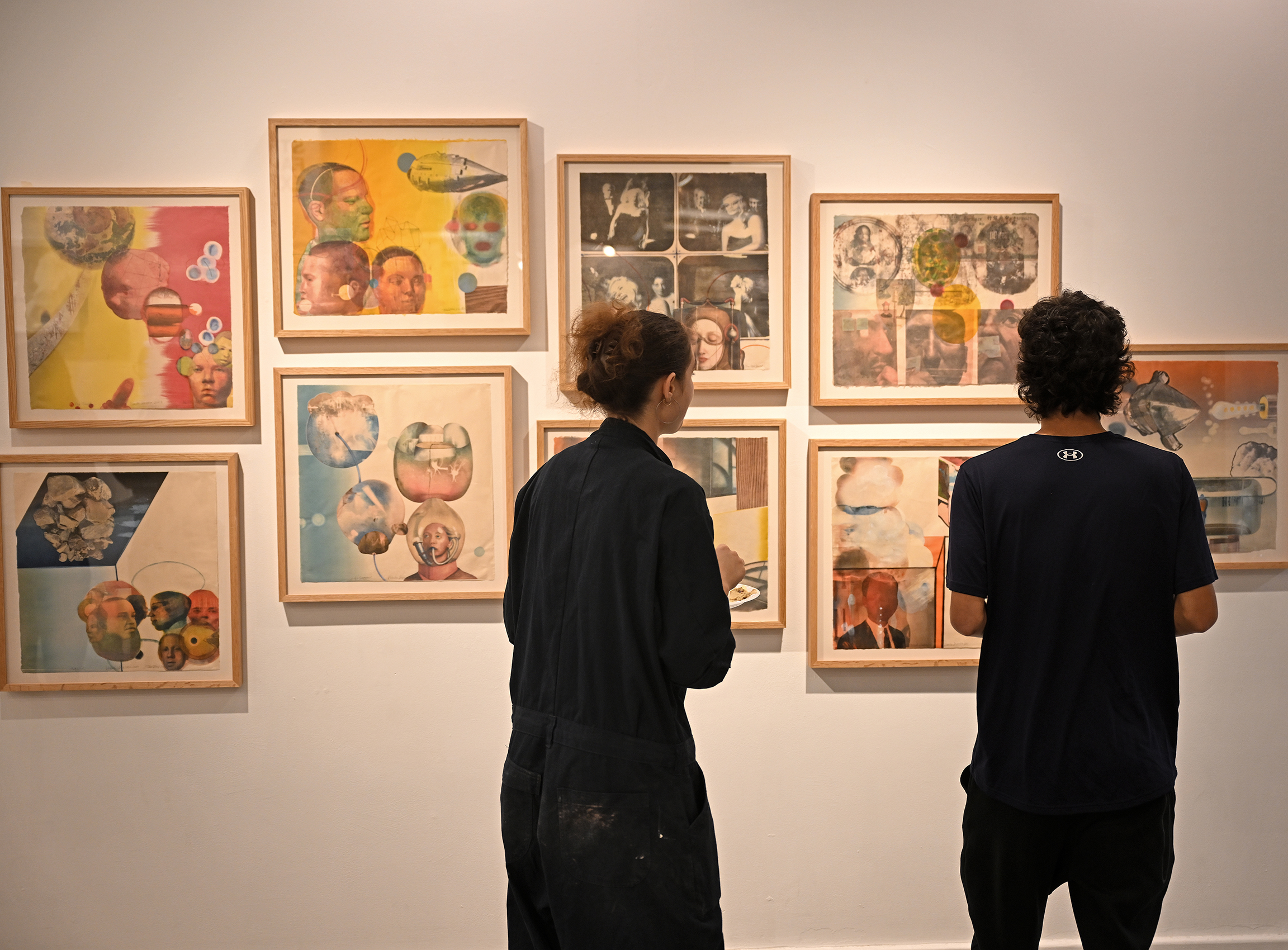 Two students view an art installation of eight framed prints during an art show opening.