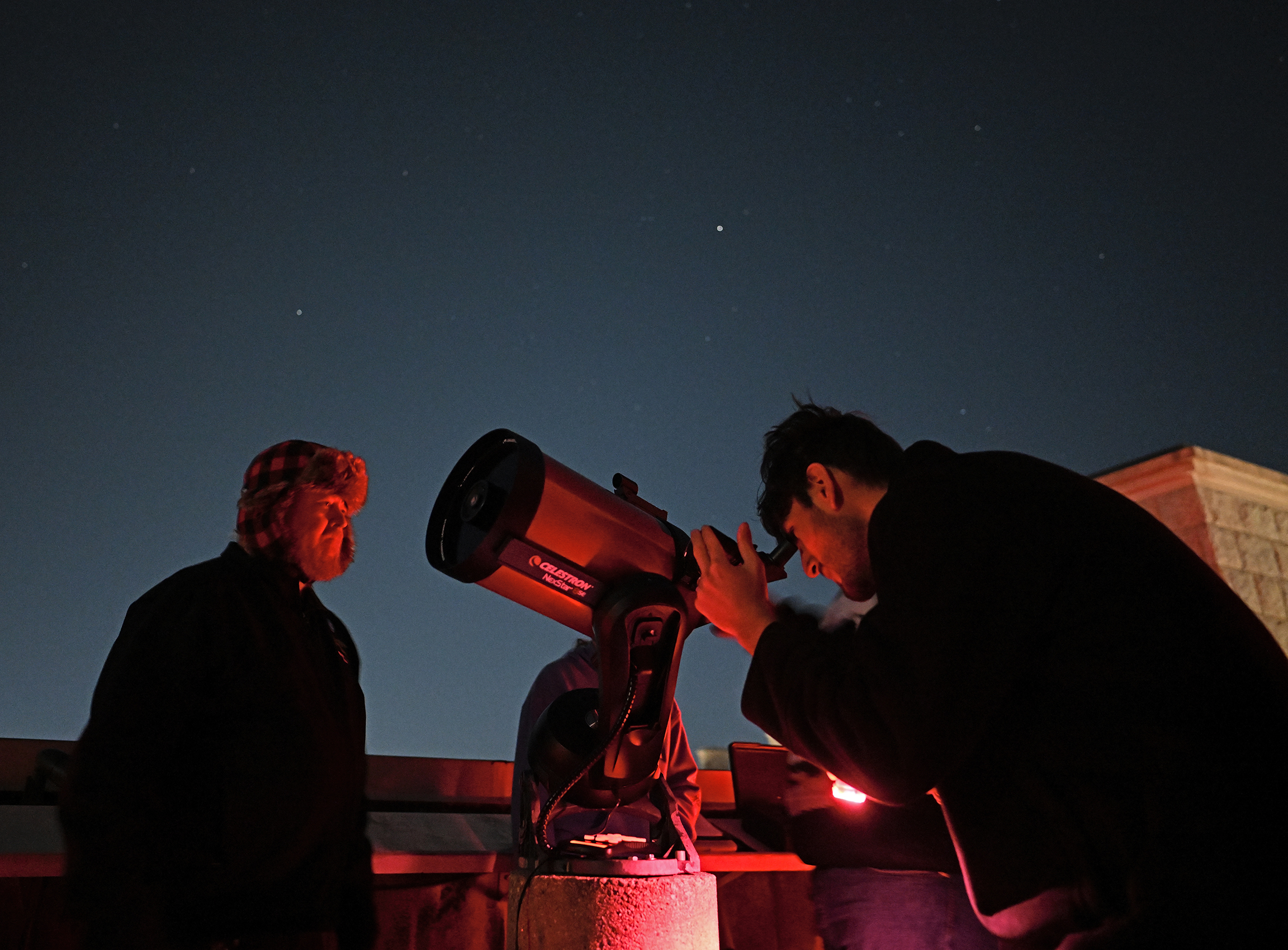 A student and professor look at the night sky with a telescope.