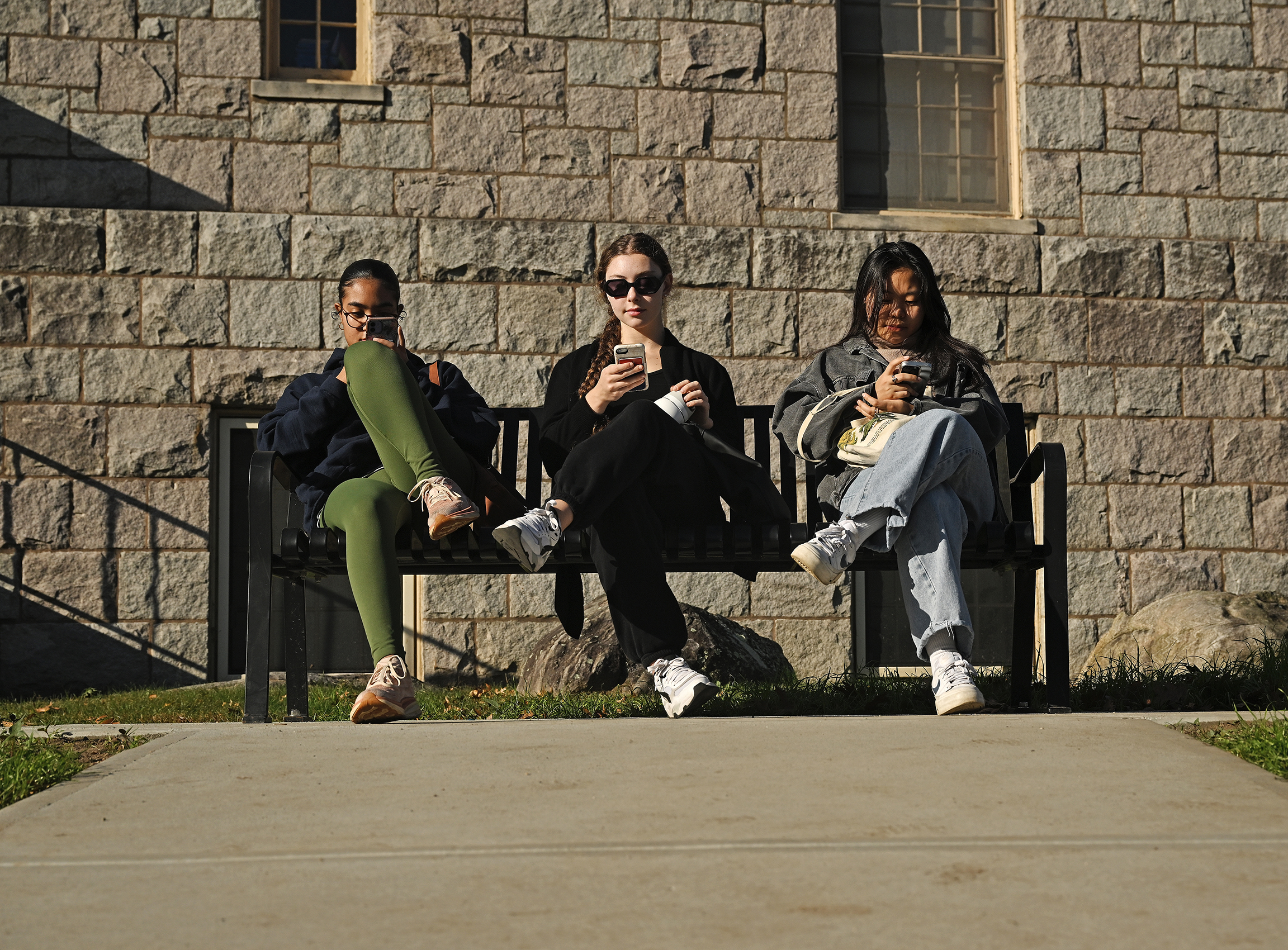 Three college students sit on a bench waiting for their ride.