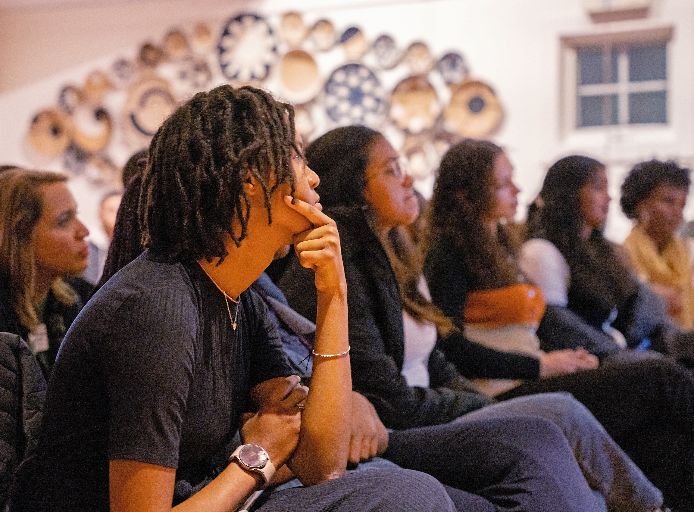 A group of students of color sit and listen to a speaker.