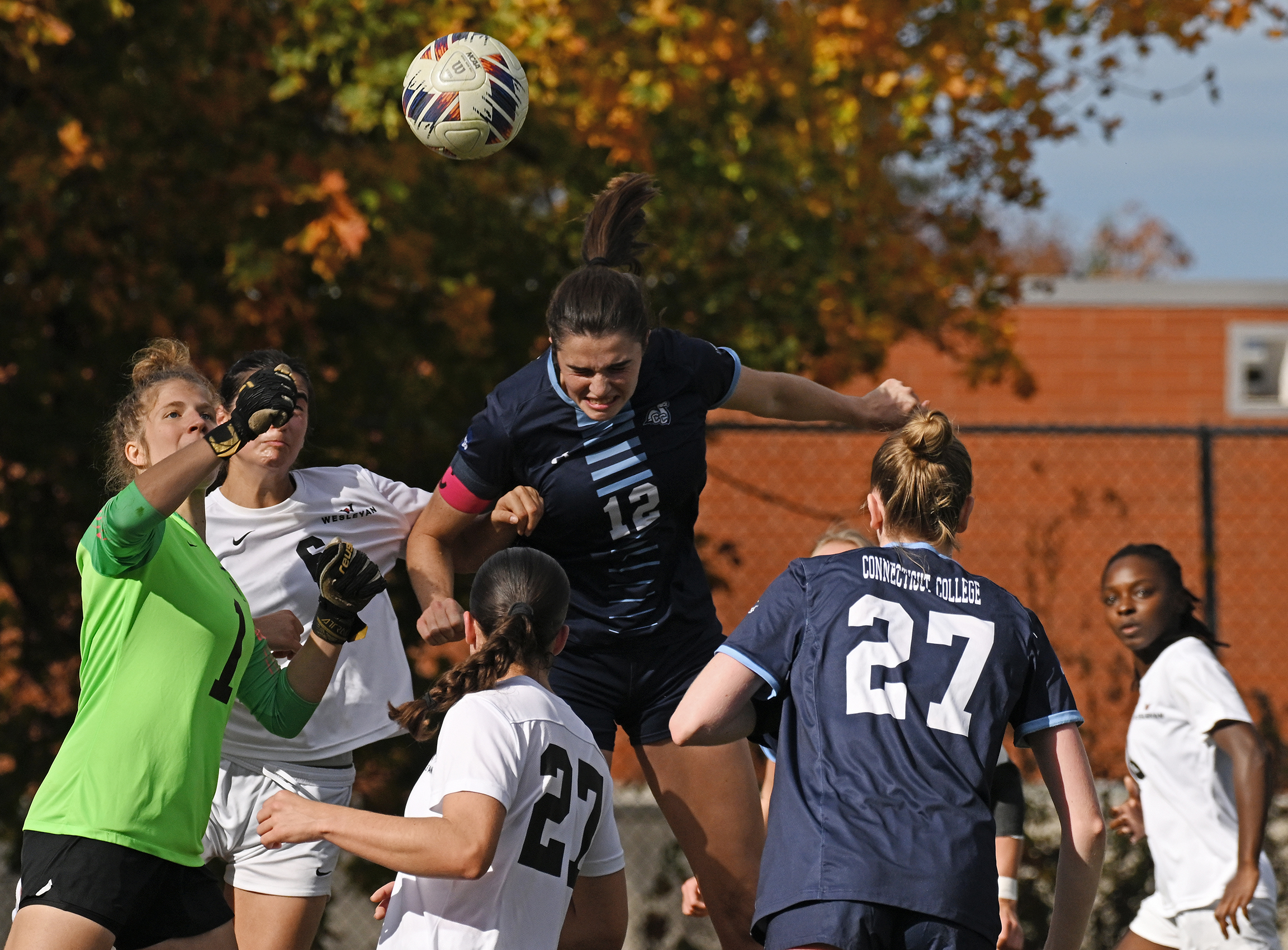 Women's soccer players leap into the air to head the ball.