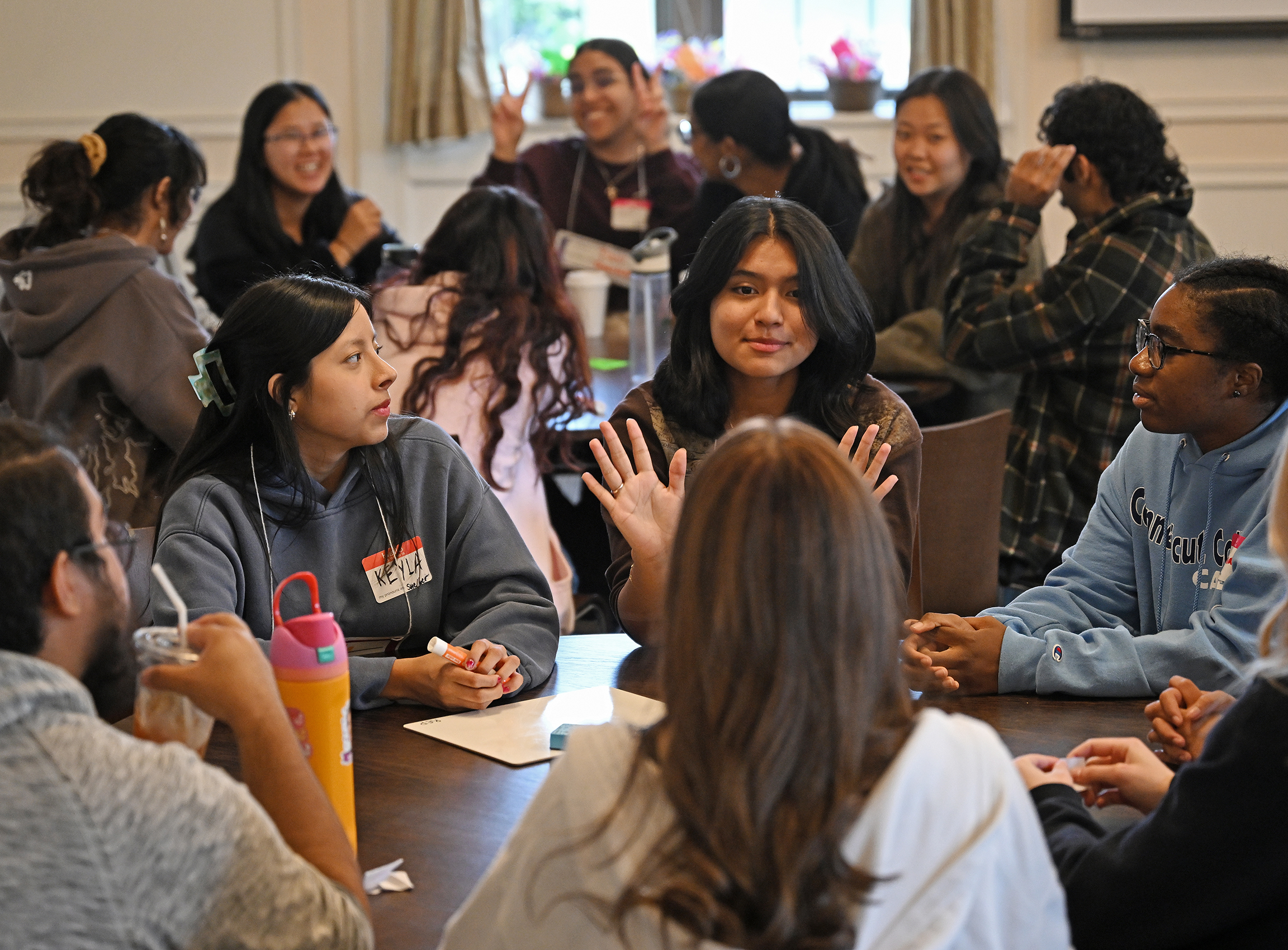 A group of students sit conversing around a circular table.