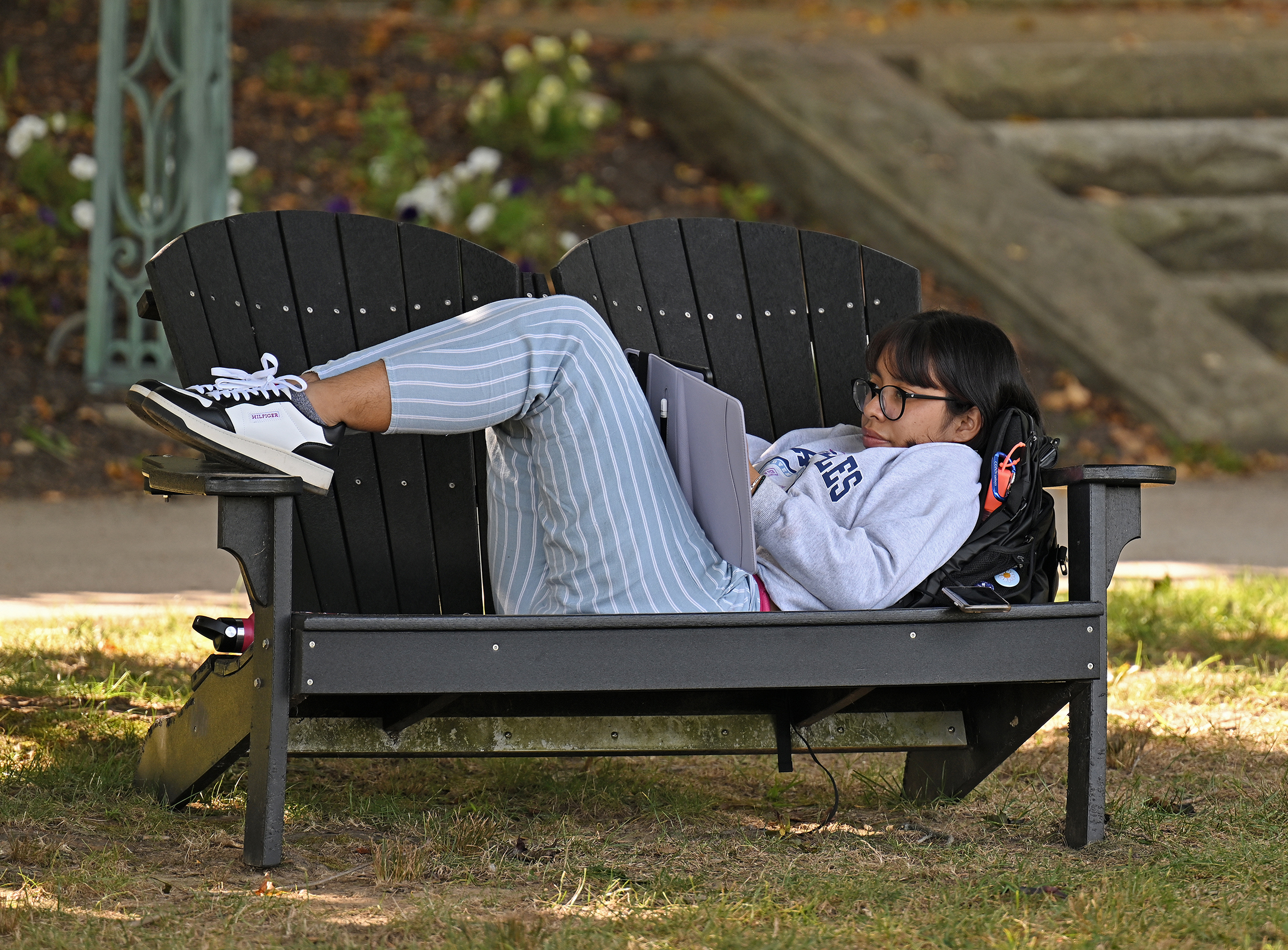 A student reclines on a double Adirondack Chair bench to view a tablet computer.