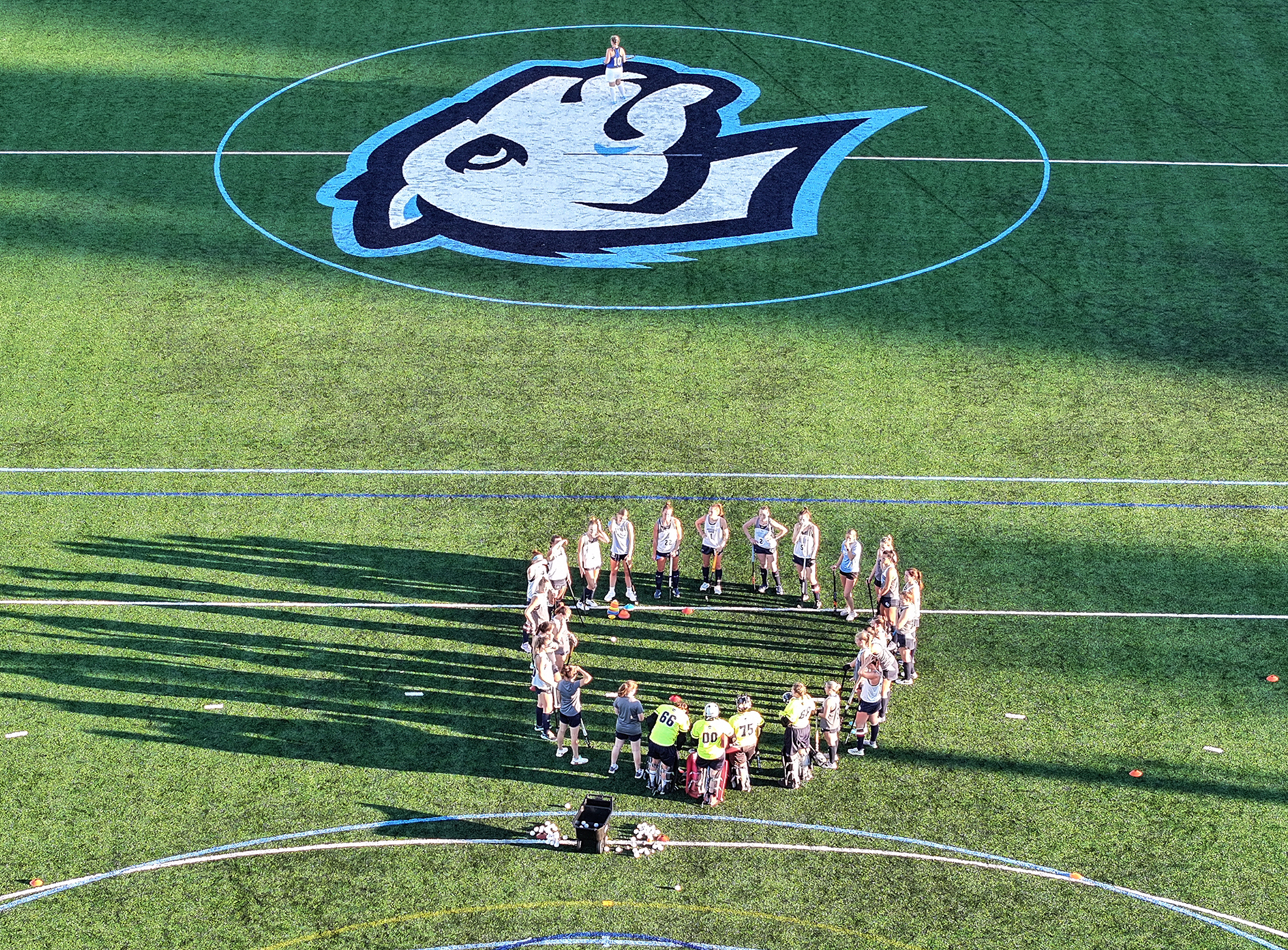 Aerial view of field hockey team huddling in late afternoon light.