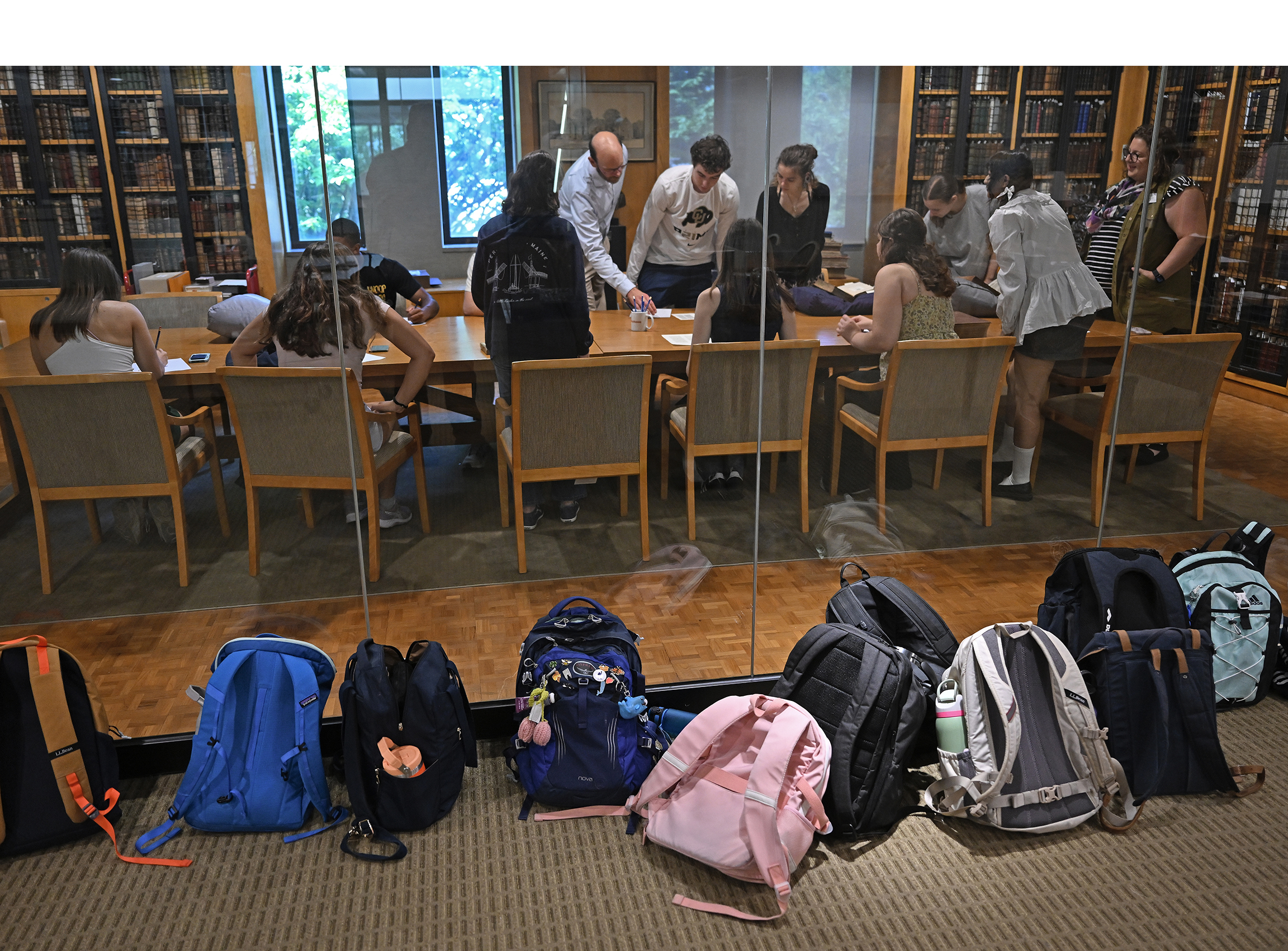 Student backpacks line a glass wall as the students visit a library special collections room on the other side