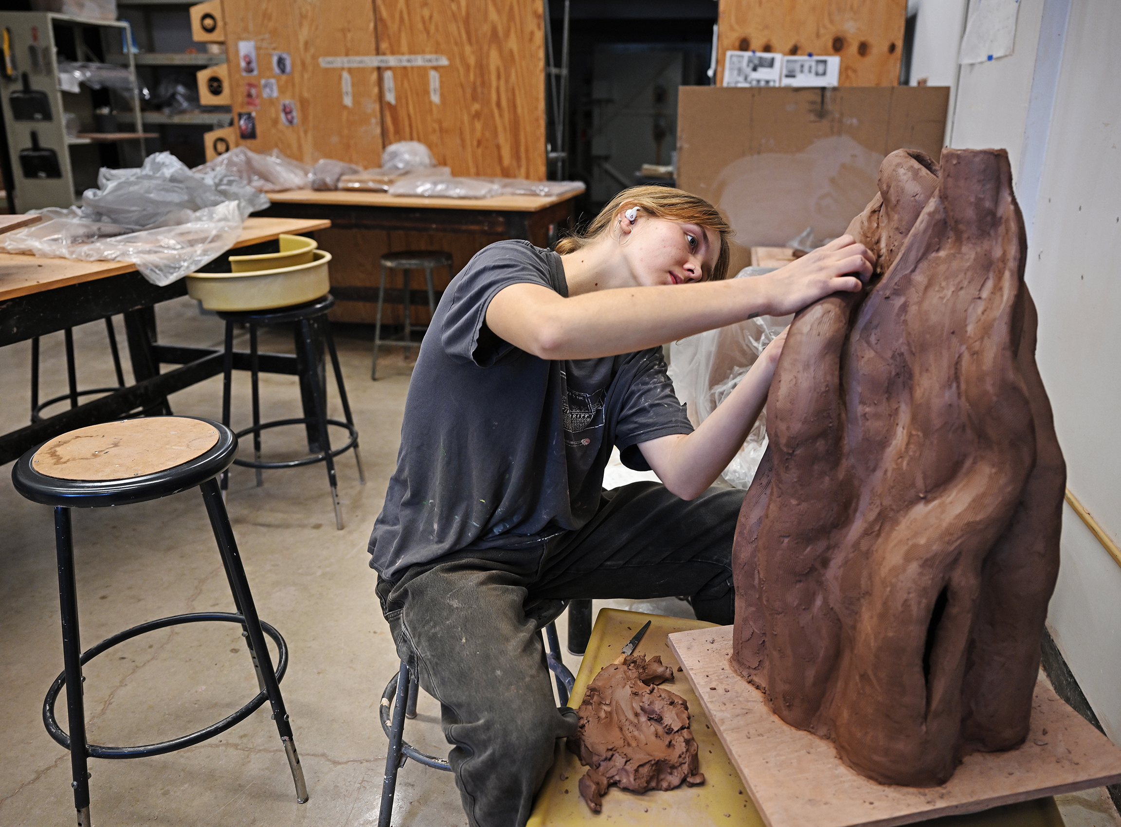 A student artists sculpts a large clay figure.