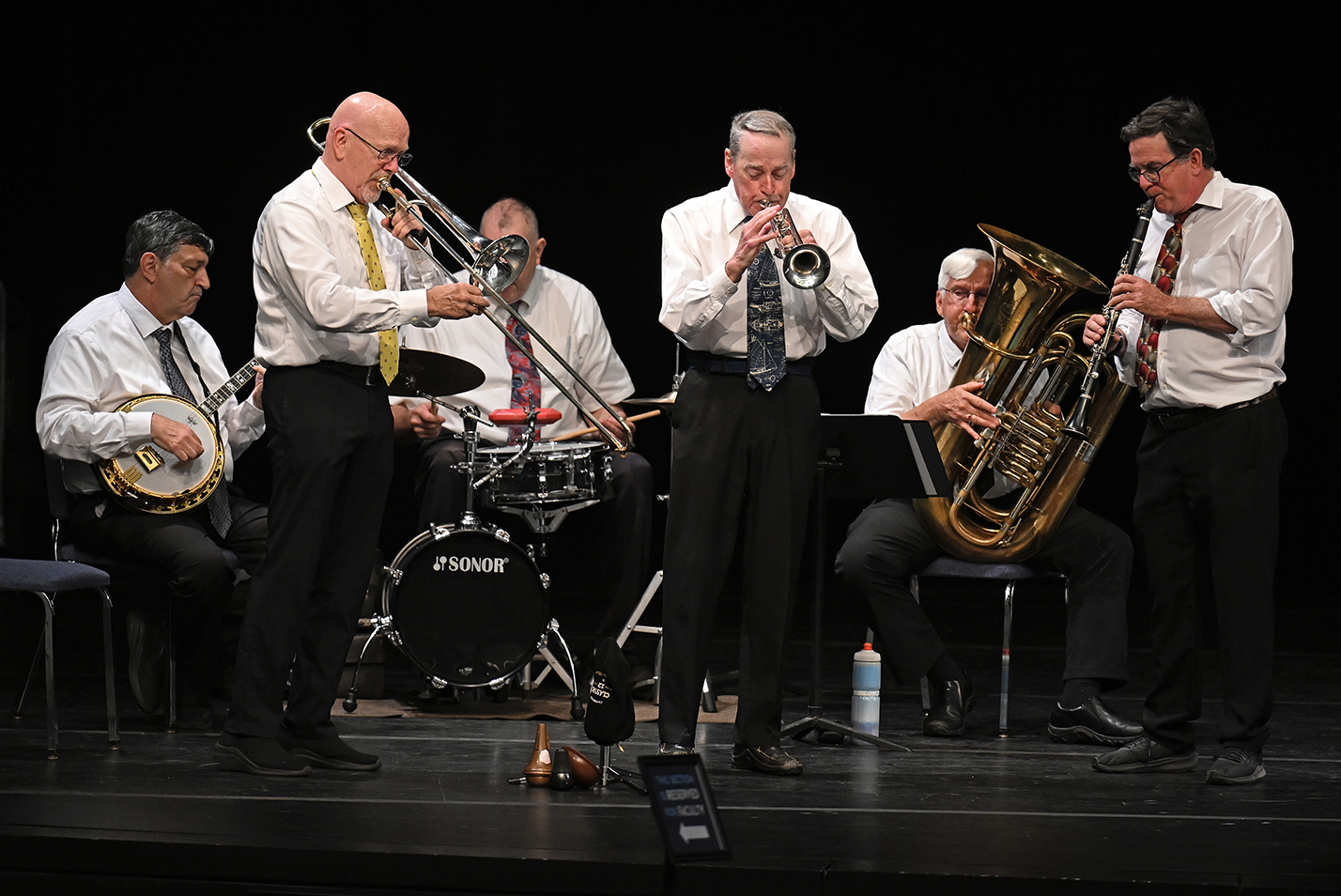 A brass band in white shirts and ties plays on a stage.