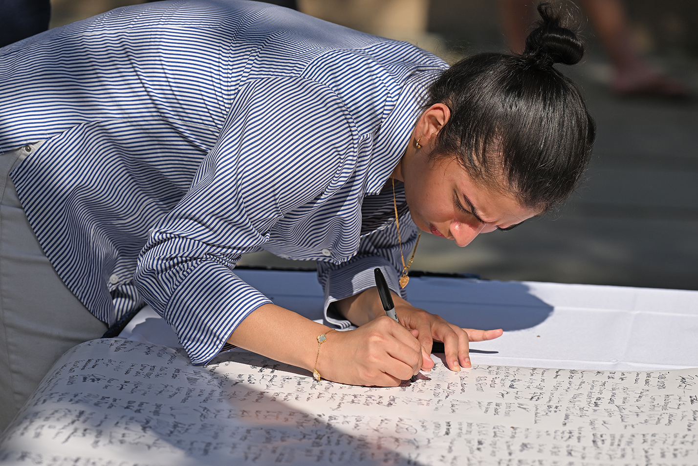 A student leans over to sign a document on a table.