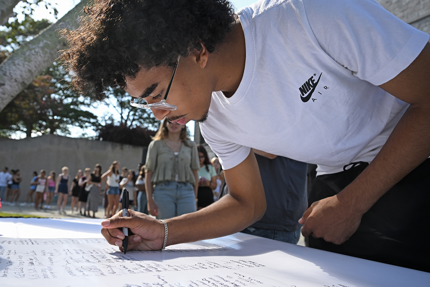 A student leans over to sign a document on a table.