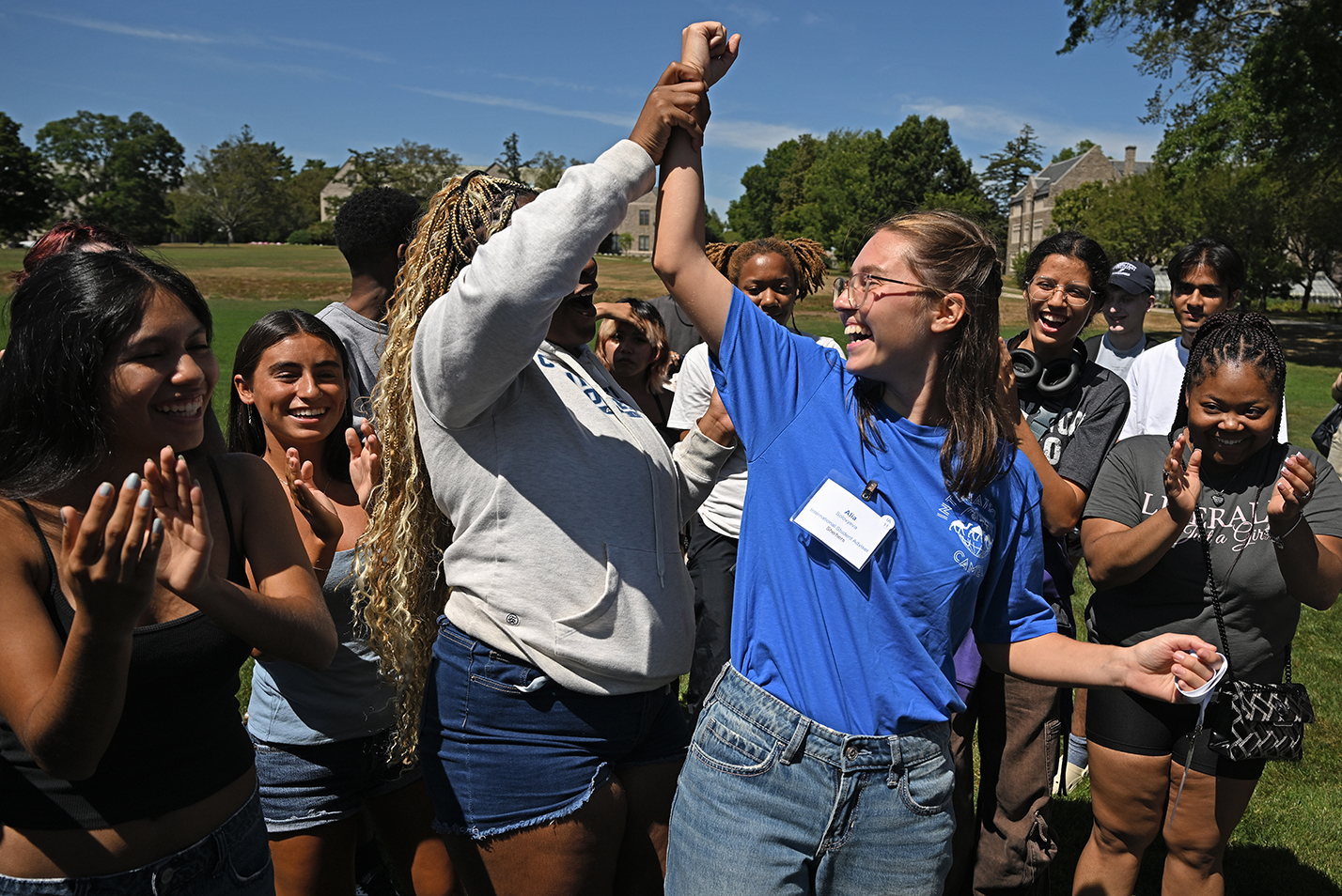 One student holds up another's arm as the winner of a friendly competition of Rock, Paper, Scissors as part of an icebreaking event on a college green.