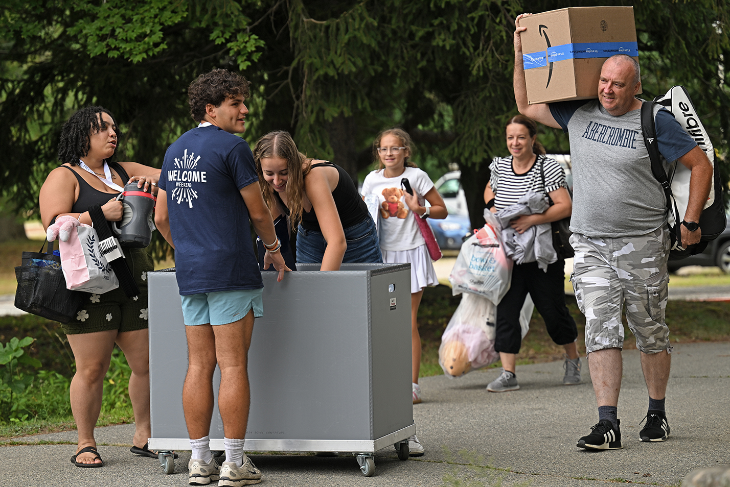 Students and their families carry, and wheel a cart of, belongings into the residence hall during a college move-in day.