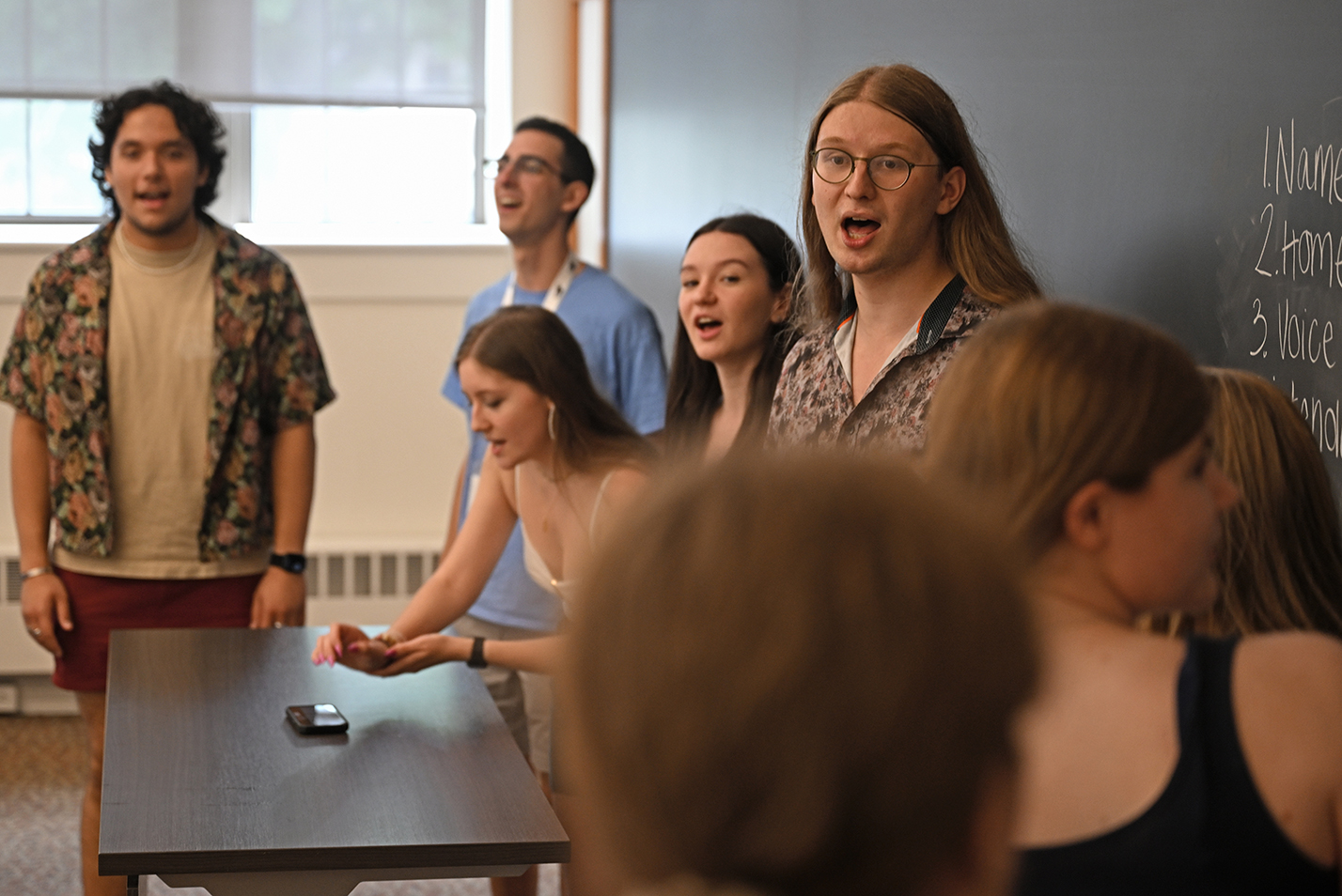 A student a cappella group leads a warm up number for a gathering of students interested in the group.