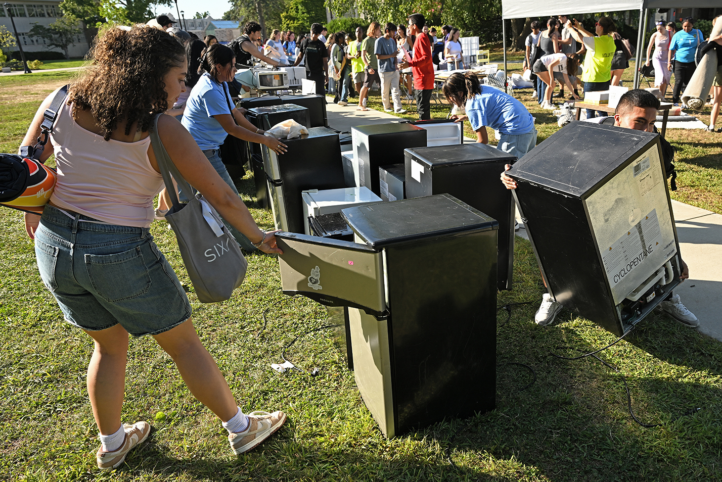College students swarm around used refrigerators at a yard sale.
