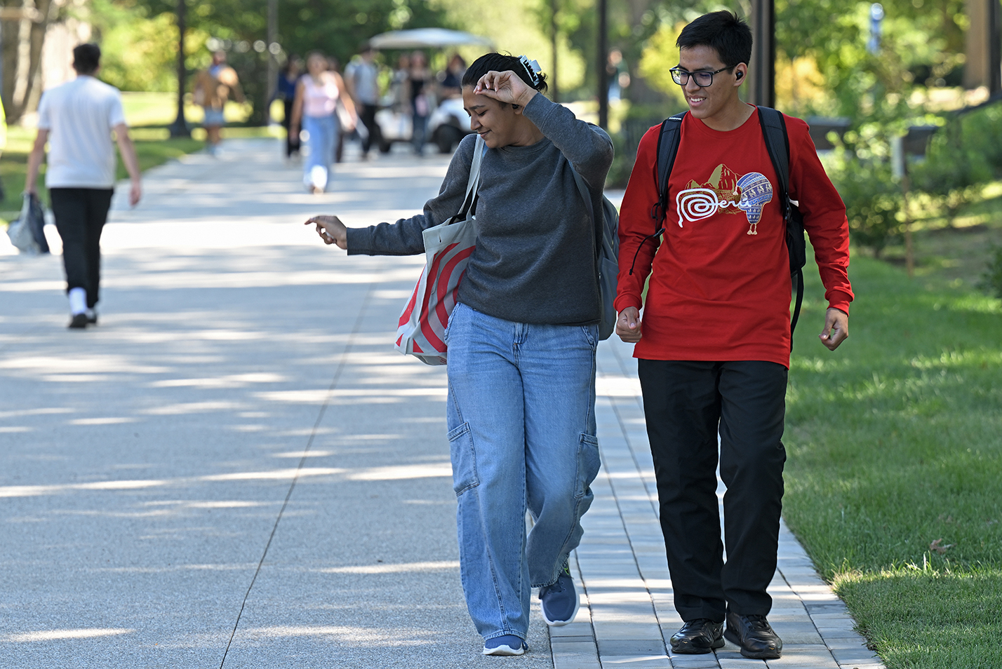 A pair of college students dance to music on their headphones as they walk along a pathway.
