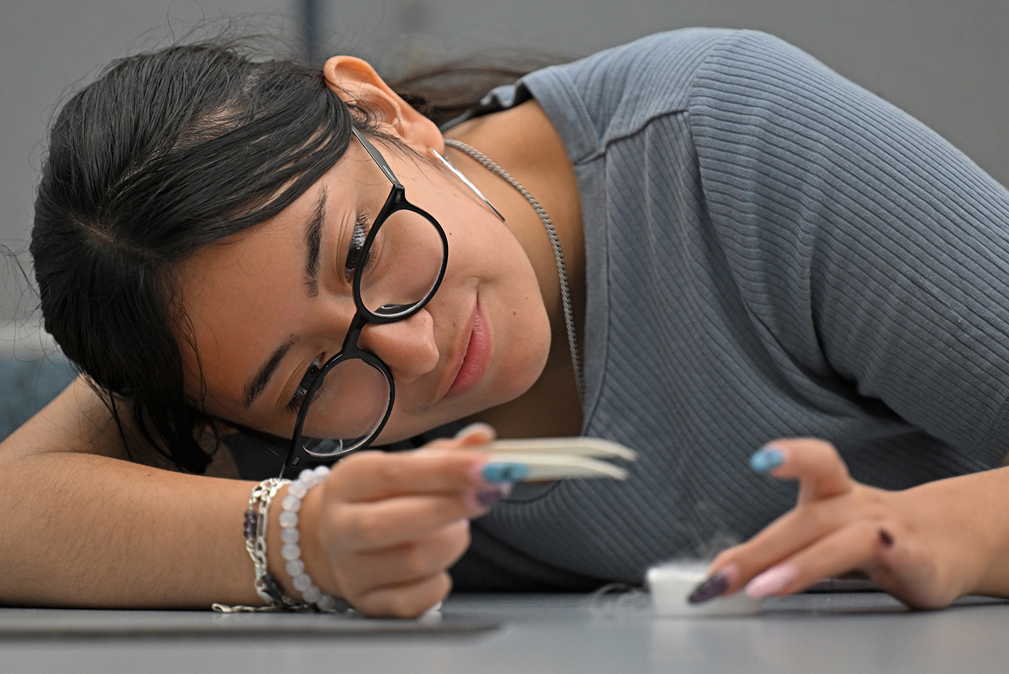 A female college student with glasses leans in to examine her experiment using a superconductor and a tiny magnet.
