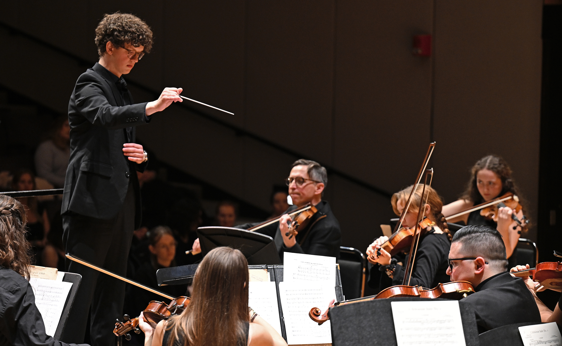 a college music student takes the baton and conducts the student orchestra on stage.