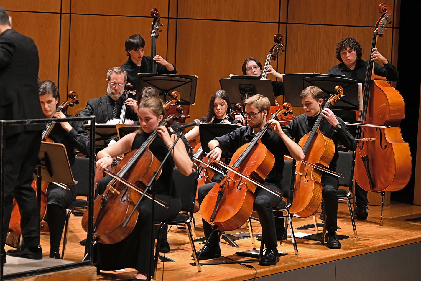 A college student orchestra performs on stage in a concert hall.