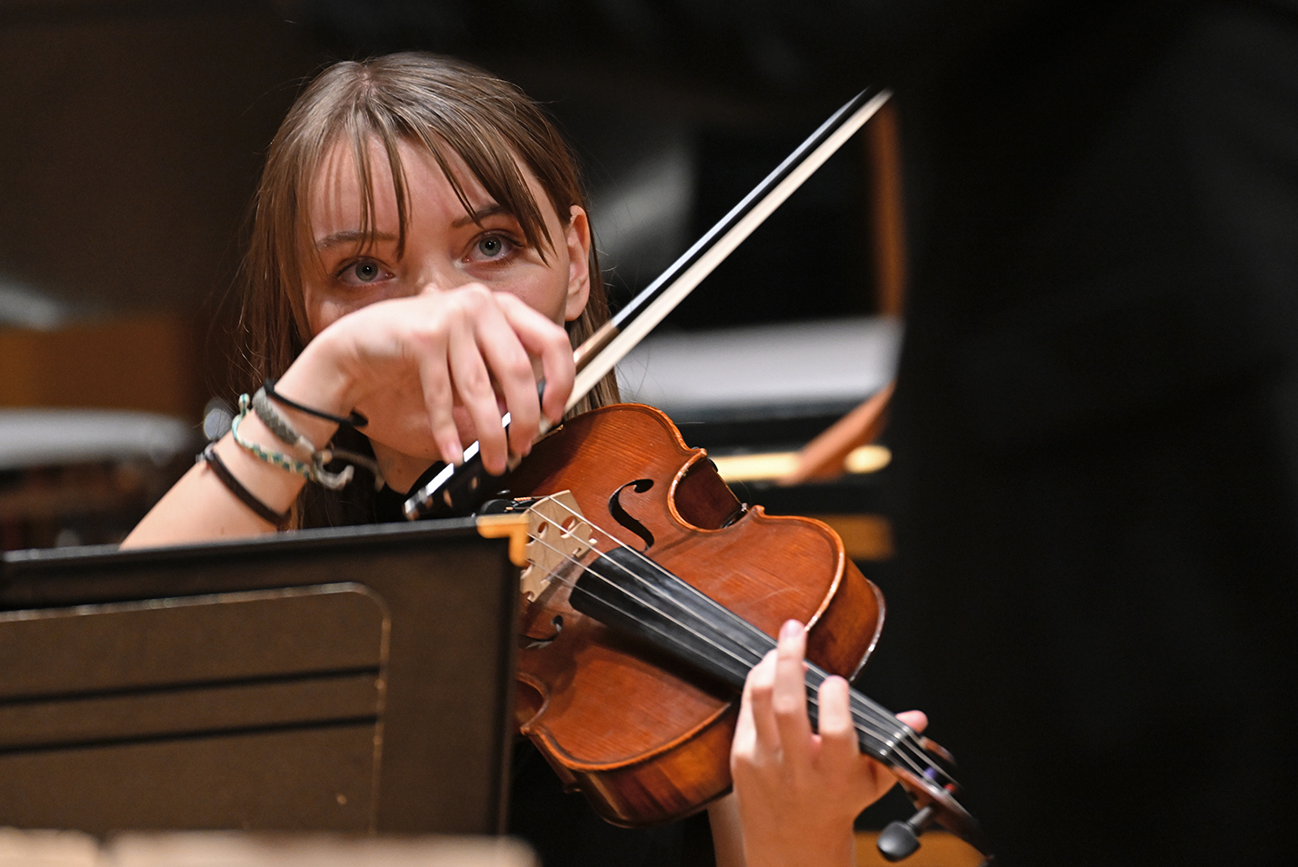A viola player looks up from her instrument for direction from the conductor during a college student orchestra concert.