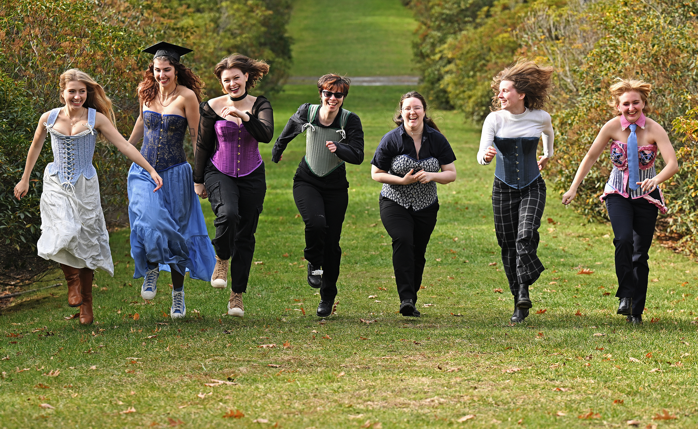 A group of college theater students skip along a green pathway wearing corsets crafted in a costuming class.