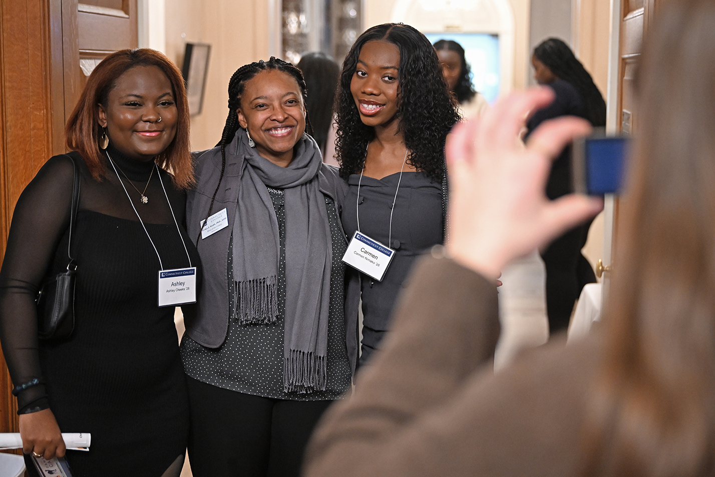 A college dean, center, takes a photo with two early graduating students.